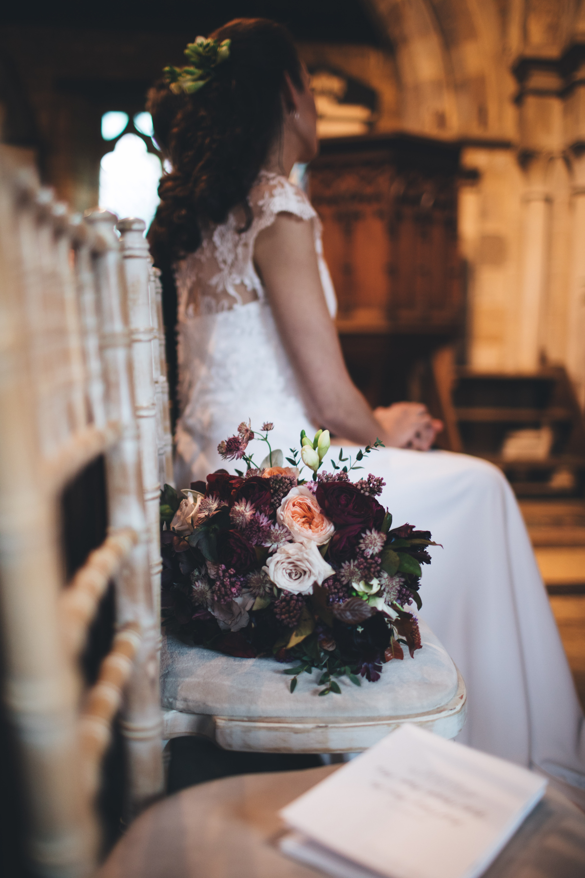 Side view of bride sitting on a chair at the front of the church with her bouquet sat on a chair next to her