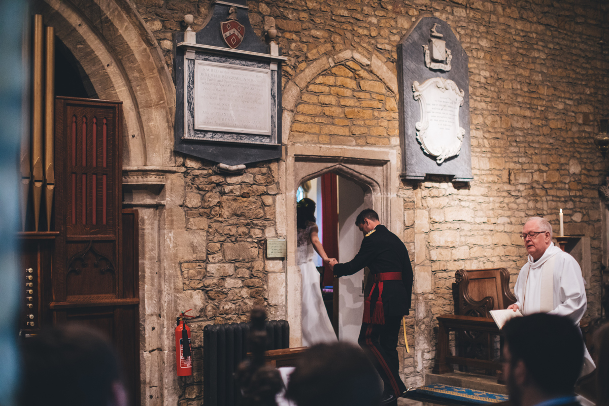 Bride and groom walking through a stone doorway in the church with the priest to the right of the shot
