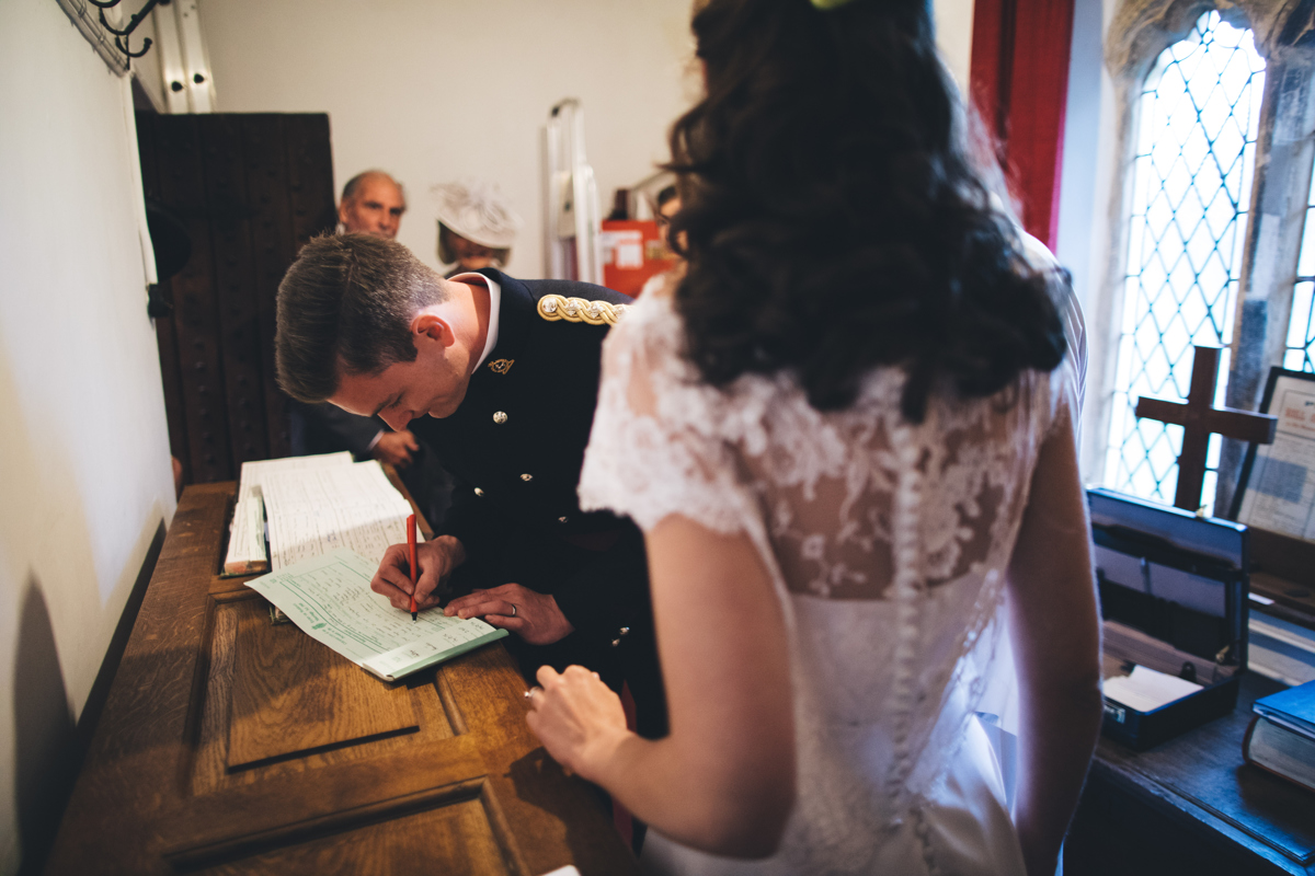 Groom bent over signing the wedding register with the brides back towards the camera