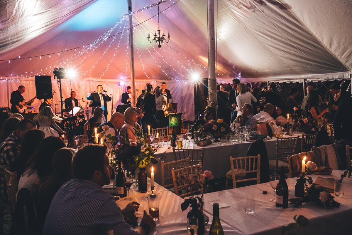 Shot of people sat at tables inside a marquee with a band and singer in the background