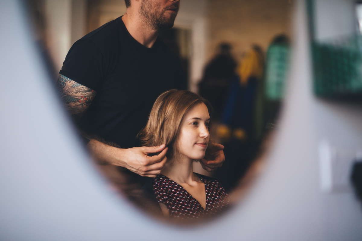 Image reflected in a mirror of a bride having her hair done by a male hairdresser