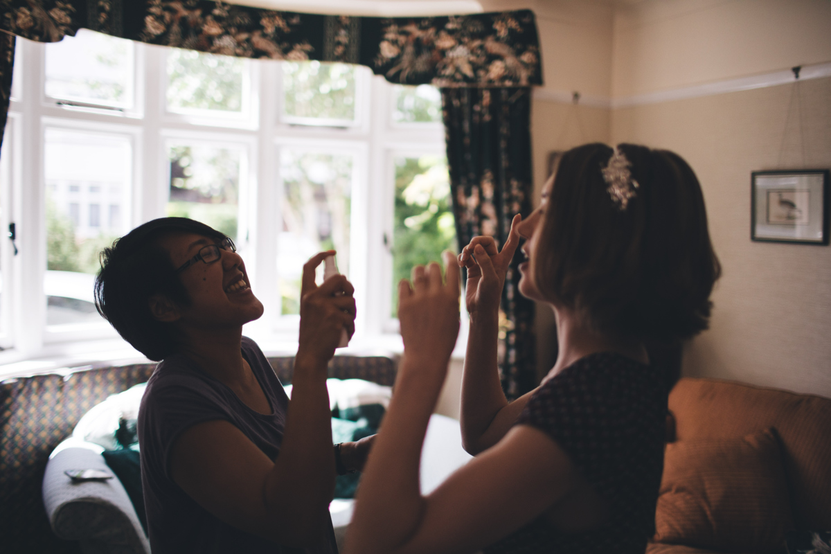 Bride and friend stood opposite each other witht he friend about to spray the bride with perfume