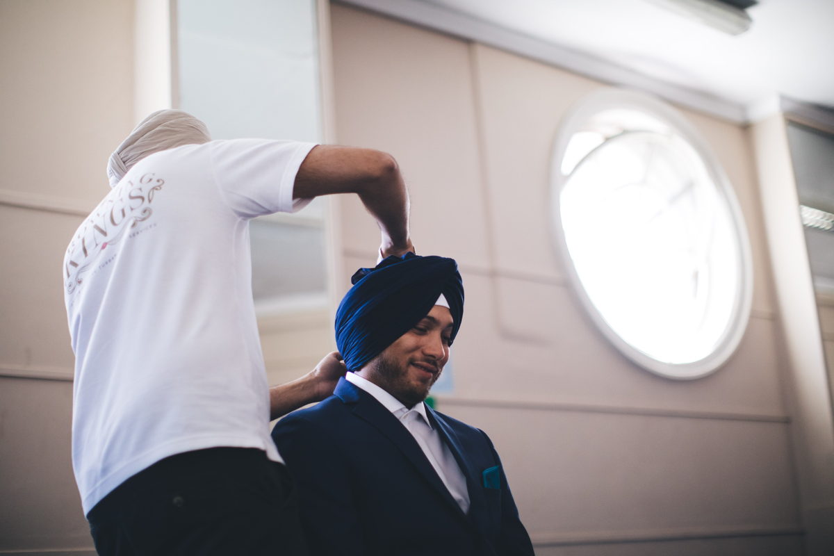 Sikh man having a blue turban tied around his head by a man in a white T-Shirt and cream coloured turban