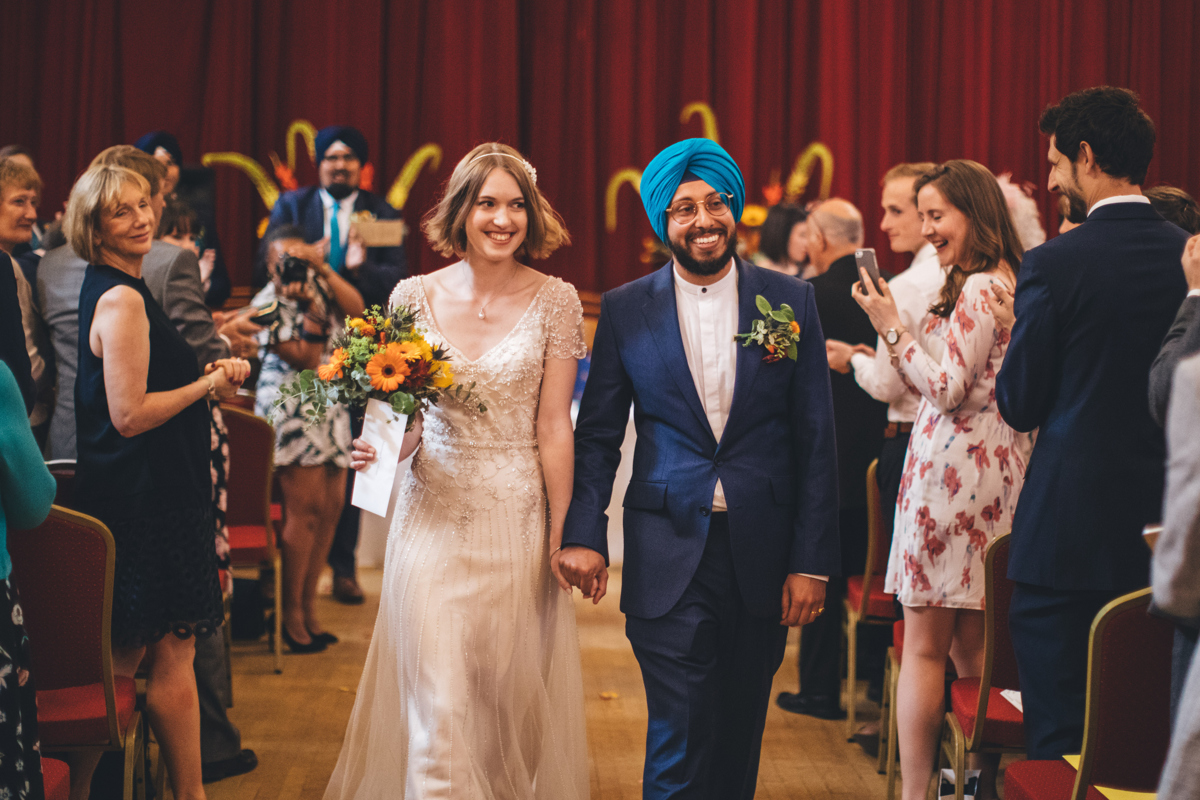 Bride and Groom walking down the aisle after getting married at Porchester Hall London with members of the wedding party looking and and taking pictures