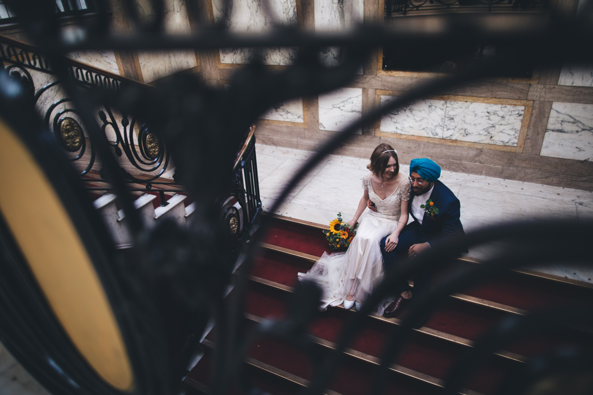 View from above looking down through the balustrade at the bride and groom sat on the stairs at Porchester Hall London