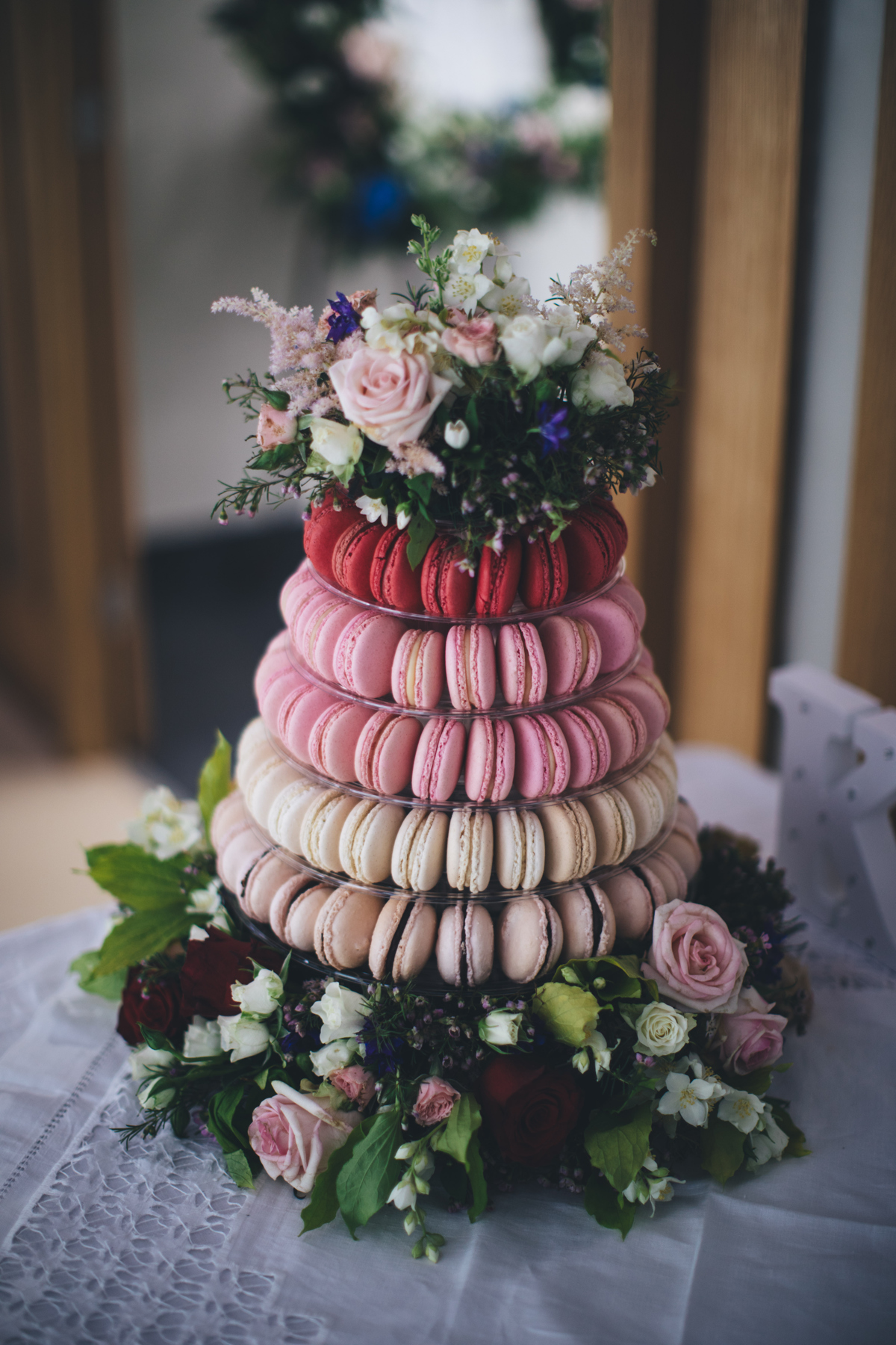 Wedding cake made up of five tiers of Macarons in pink hues from red to cream with flowers around the base and on top