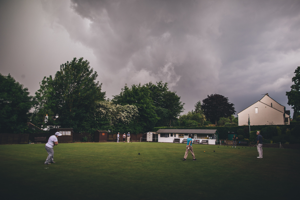 Bowling green with people playing bowls in Bardsey Village, Leeds. There are large trees in the background and grey clouds in the sky