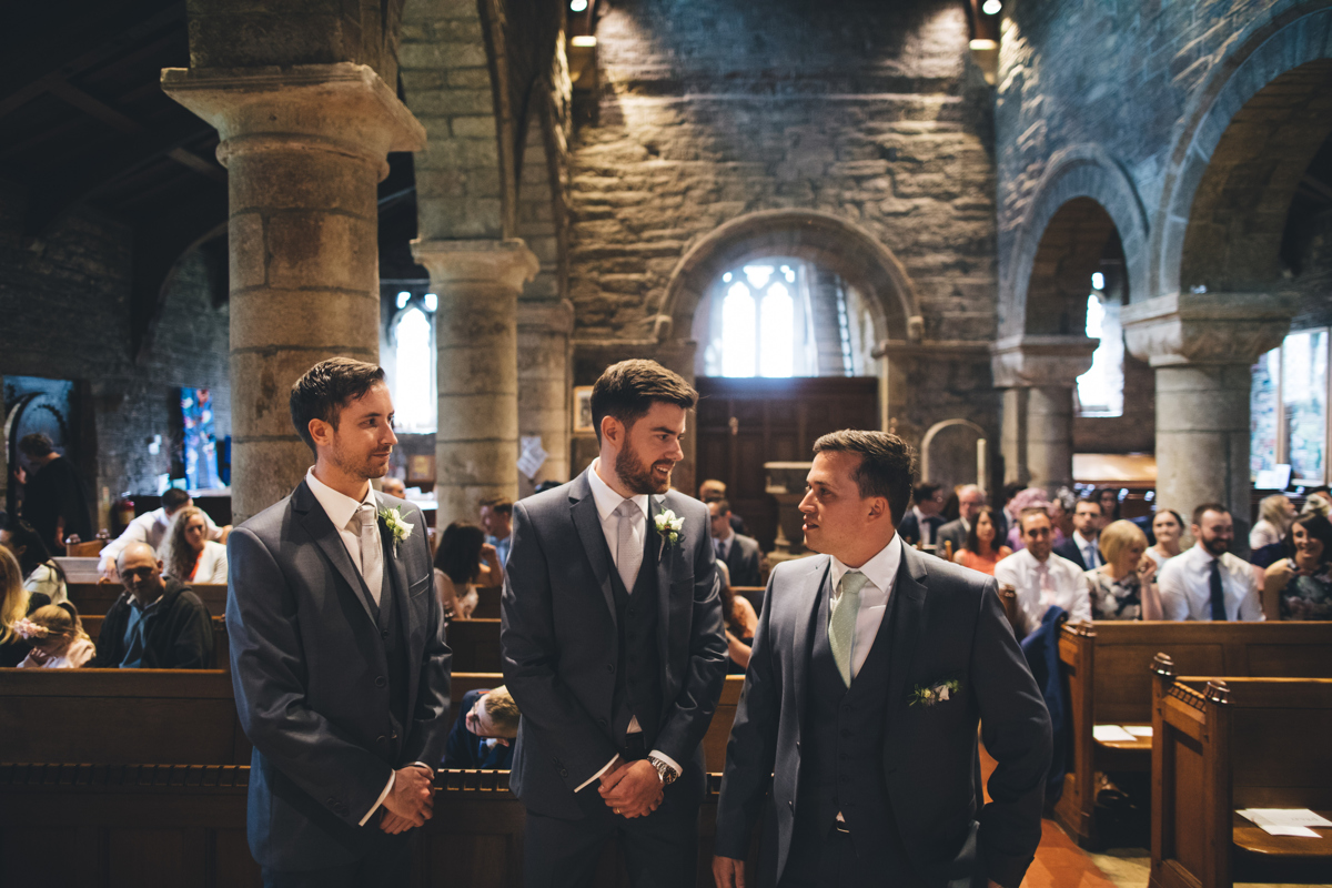 Groom and two groomsmen stood next to him at the front of the church in Bardsey, Leeds. The three men are all wearing grey three piece suits