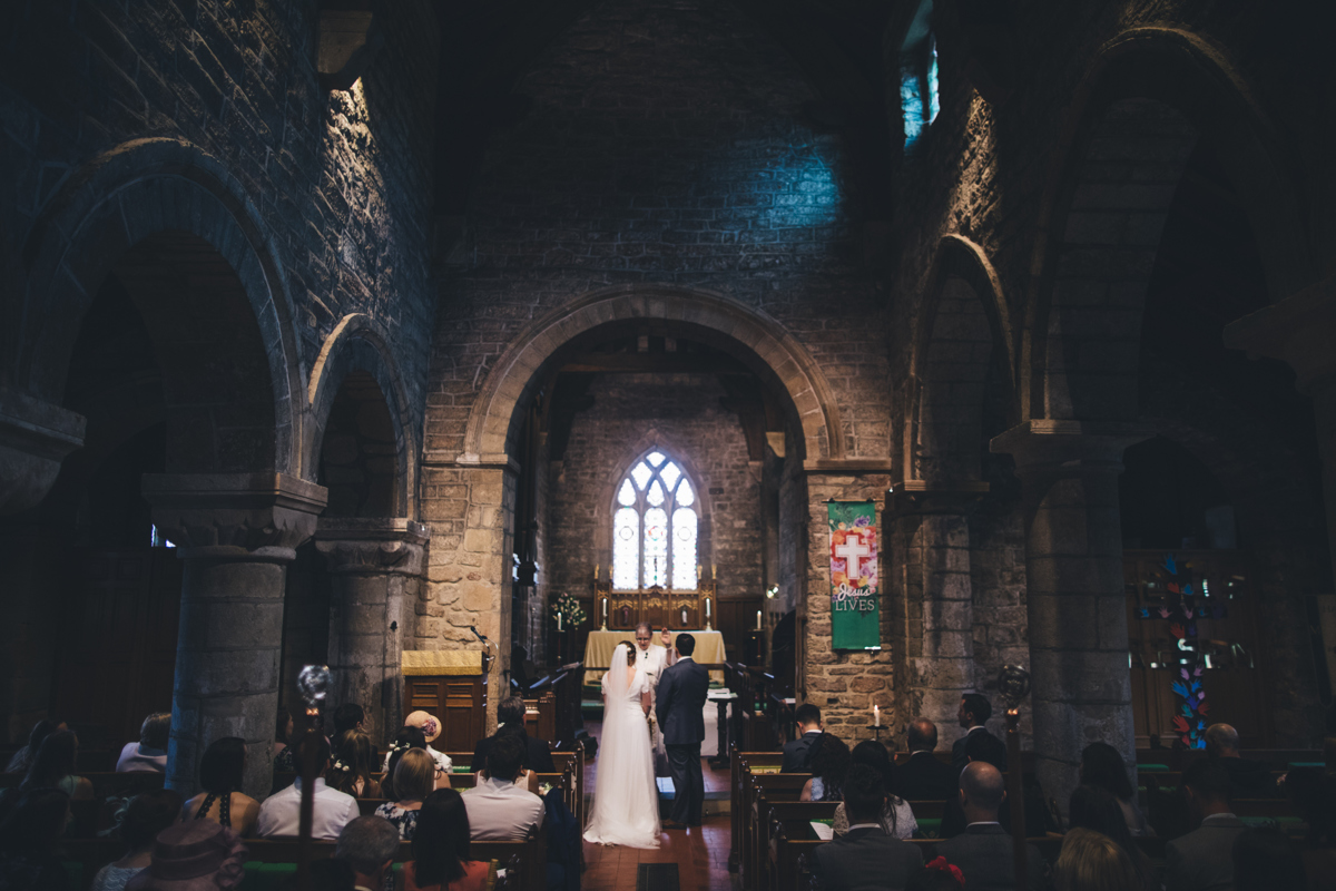 View from the back of Bardsey village church towards the front where a couple is getting married, stood in front of a priest