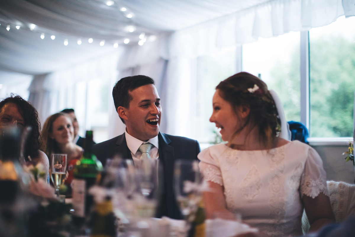 Bride and groom seated looking at each other smiling at their wedding reception in Bardsey Village Hall, Leeds