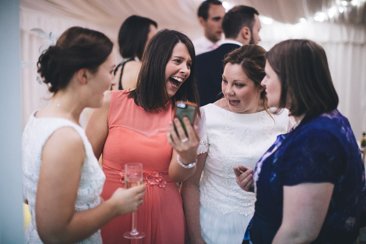 Bride and three wedding guests laughing, looking at a mobile phone