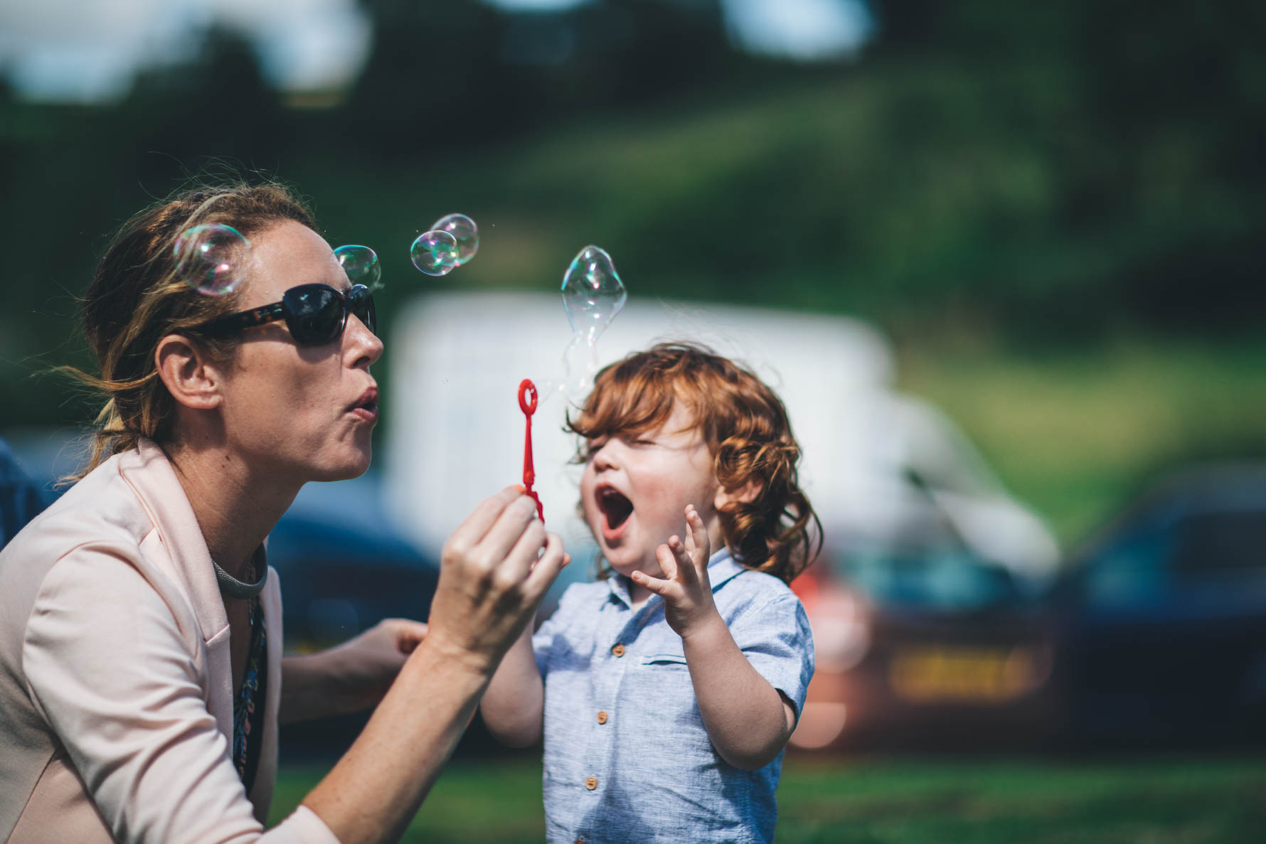 Woman blowing bubbles with a young boy with ginger hair about to catch the bubbles