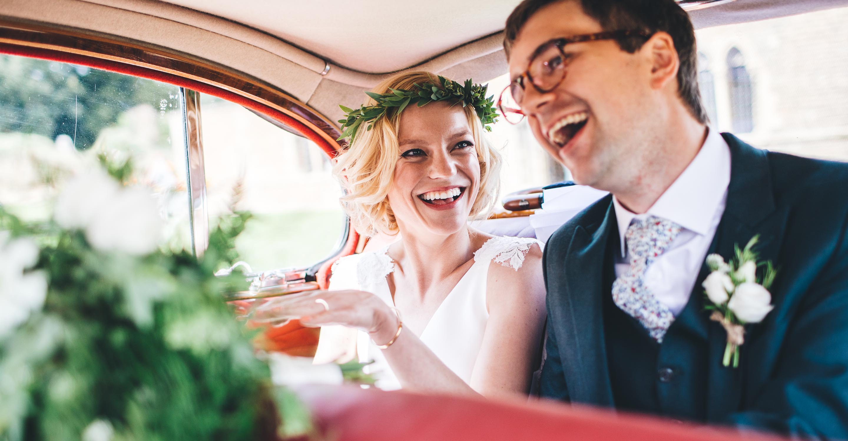 Bride and Groom sat in the back of a vintage wedding car with big smiles on their faces