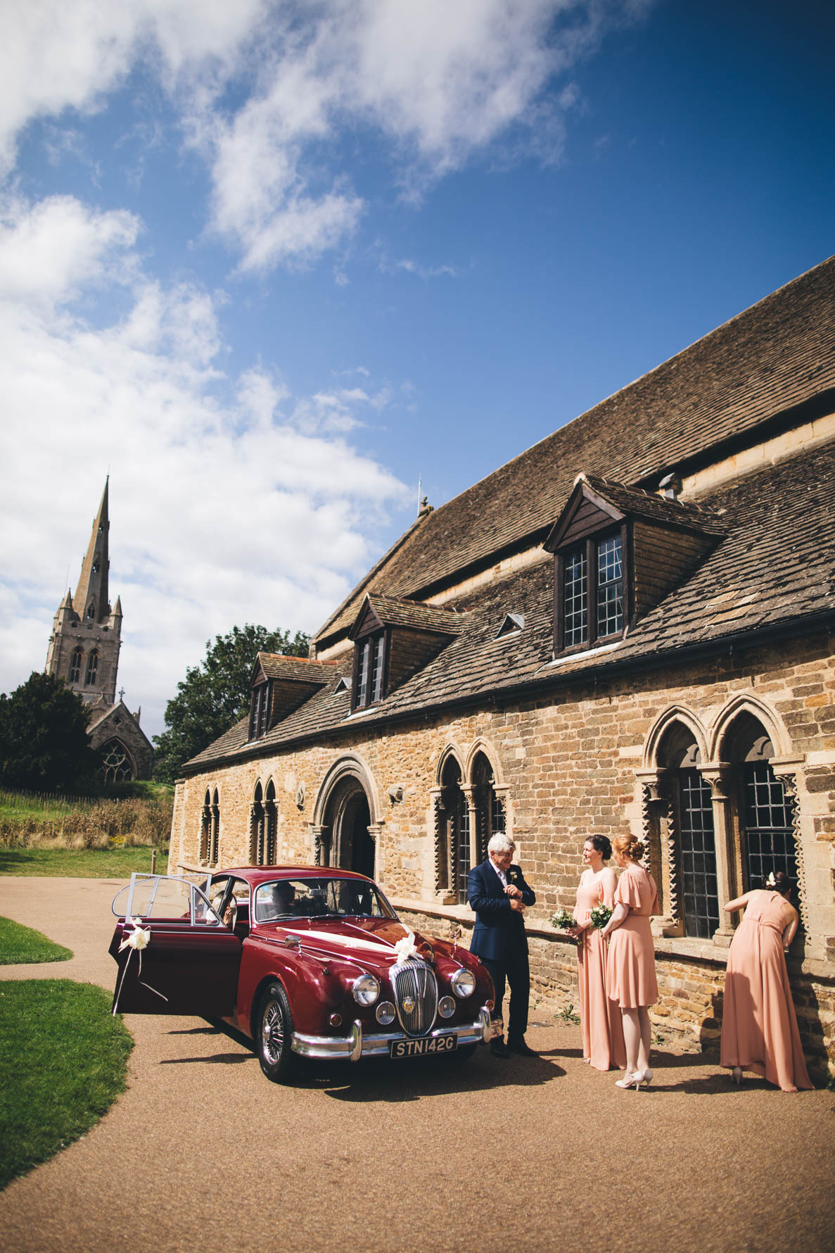 Three bridesmaids greeting the bride and her father in a vintage red car at the Great Hall at Oakham Castle
