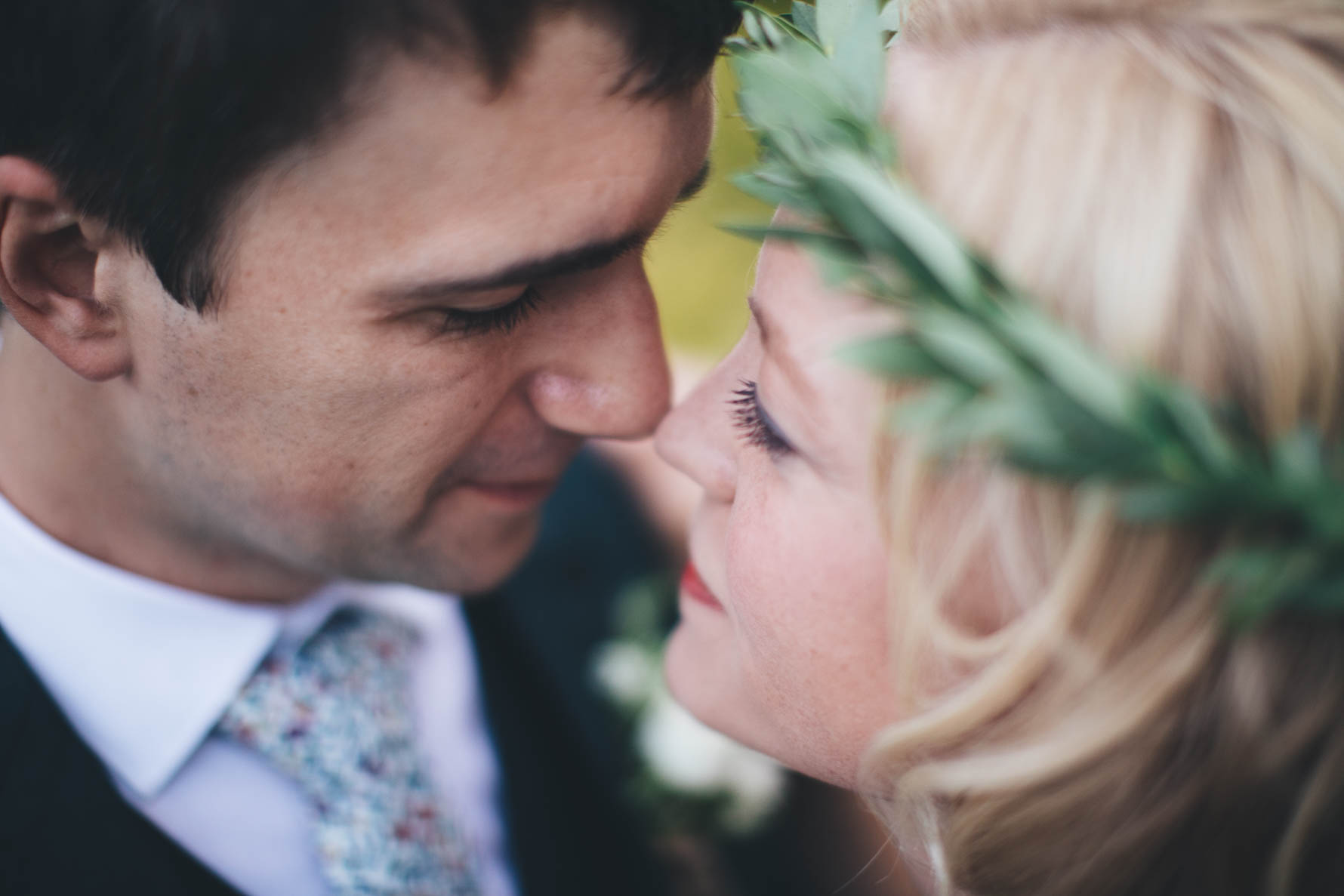 Close up of a bride and groom touching their noses together. The bride had a leaf garland around her head