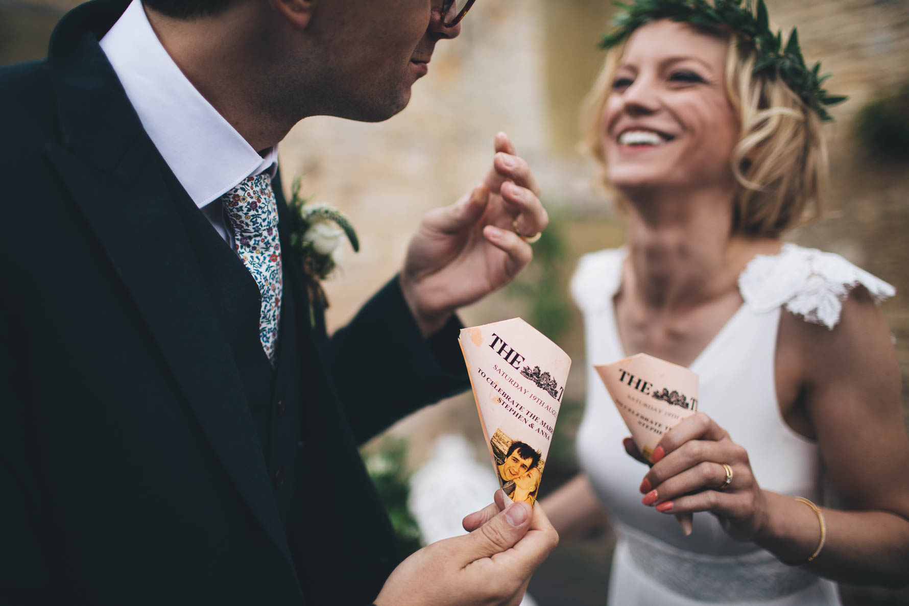 Bride and groom laughing, eating chips out of small cones made out of newspaper which they are holding