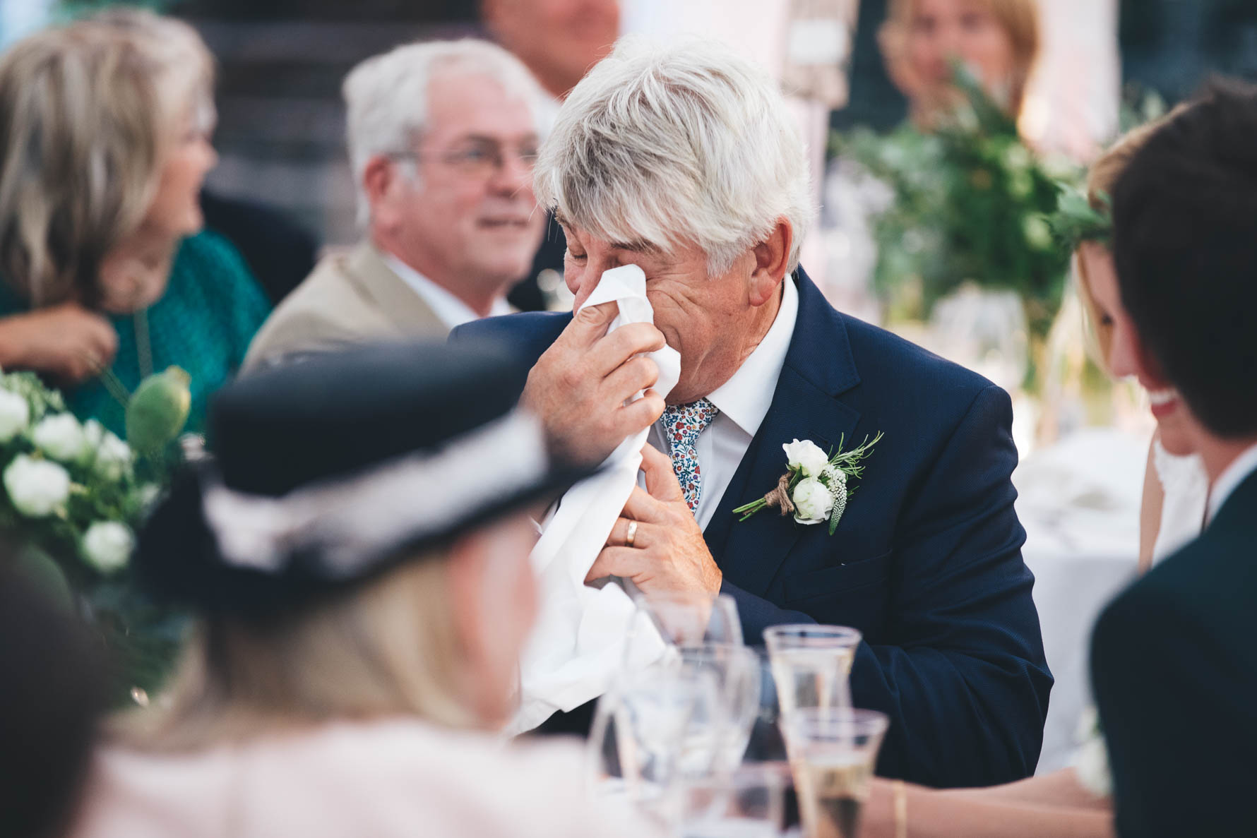 Father of the bride wiping a tear away from his eye with a napkin during the speeches at a wedding.