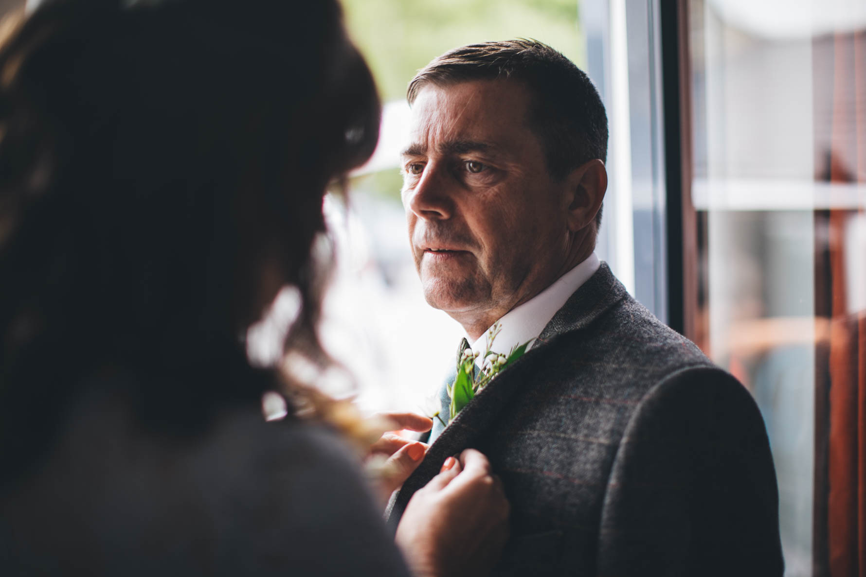 Father of the bride having his buttonhole put onto his suit lapel by the bride