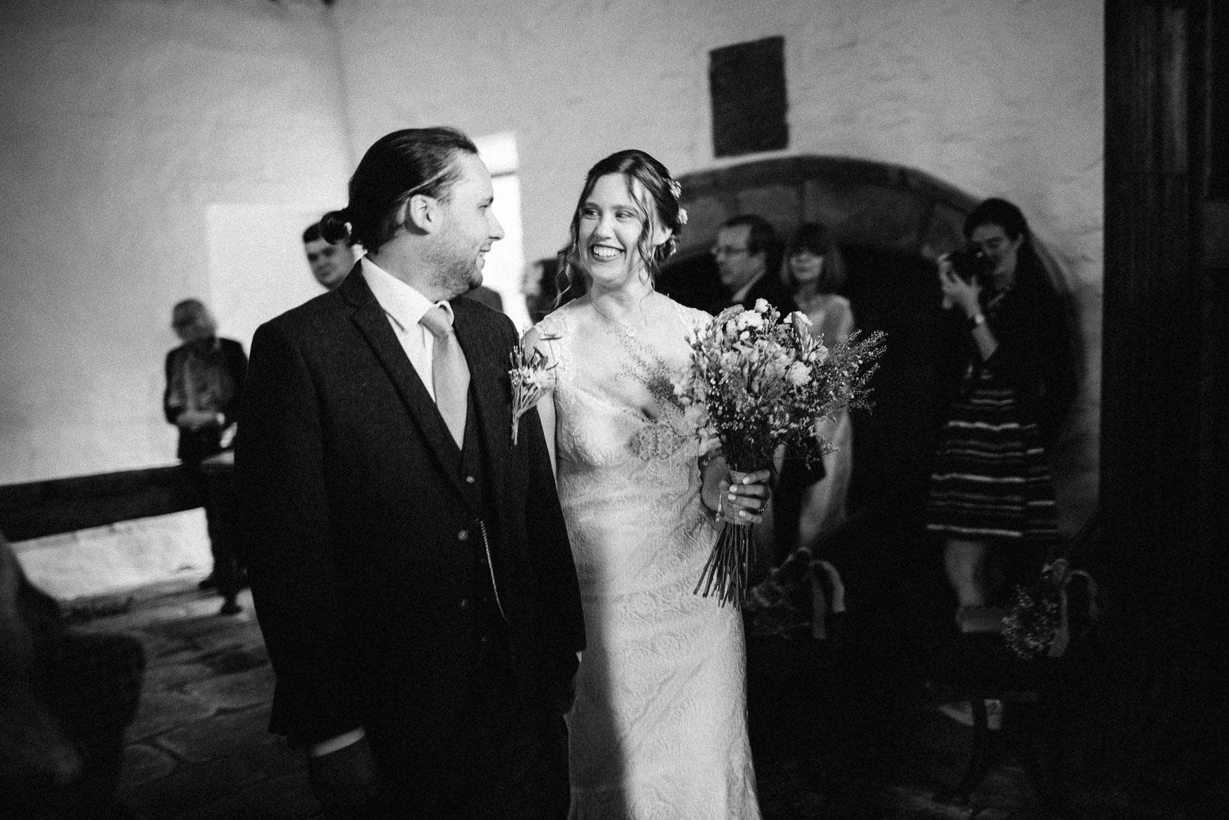 Black and white shot of of the bride and groom smiling at each other as they walk down the aisle after their wedding ceremony
