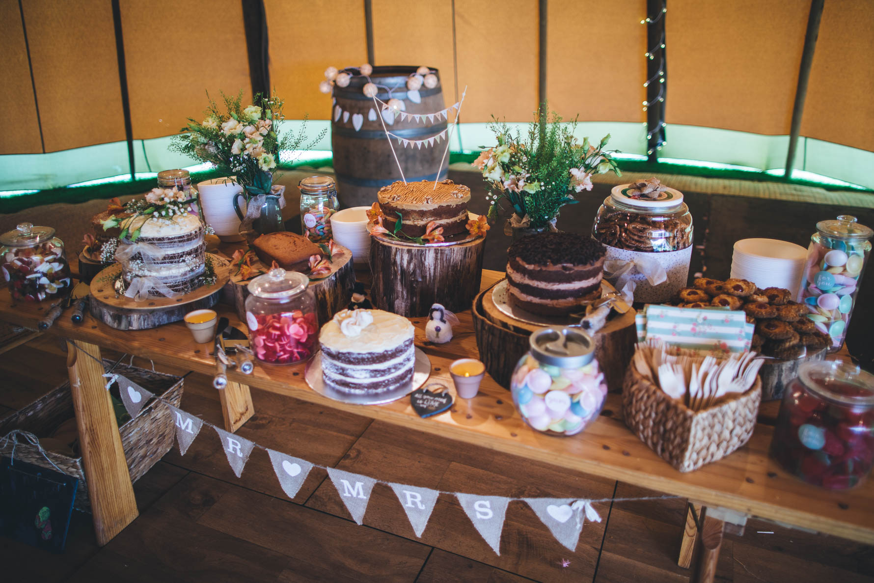 Table inside a tipi filled with cakes and sweets for a wedding reception