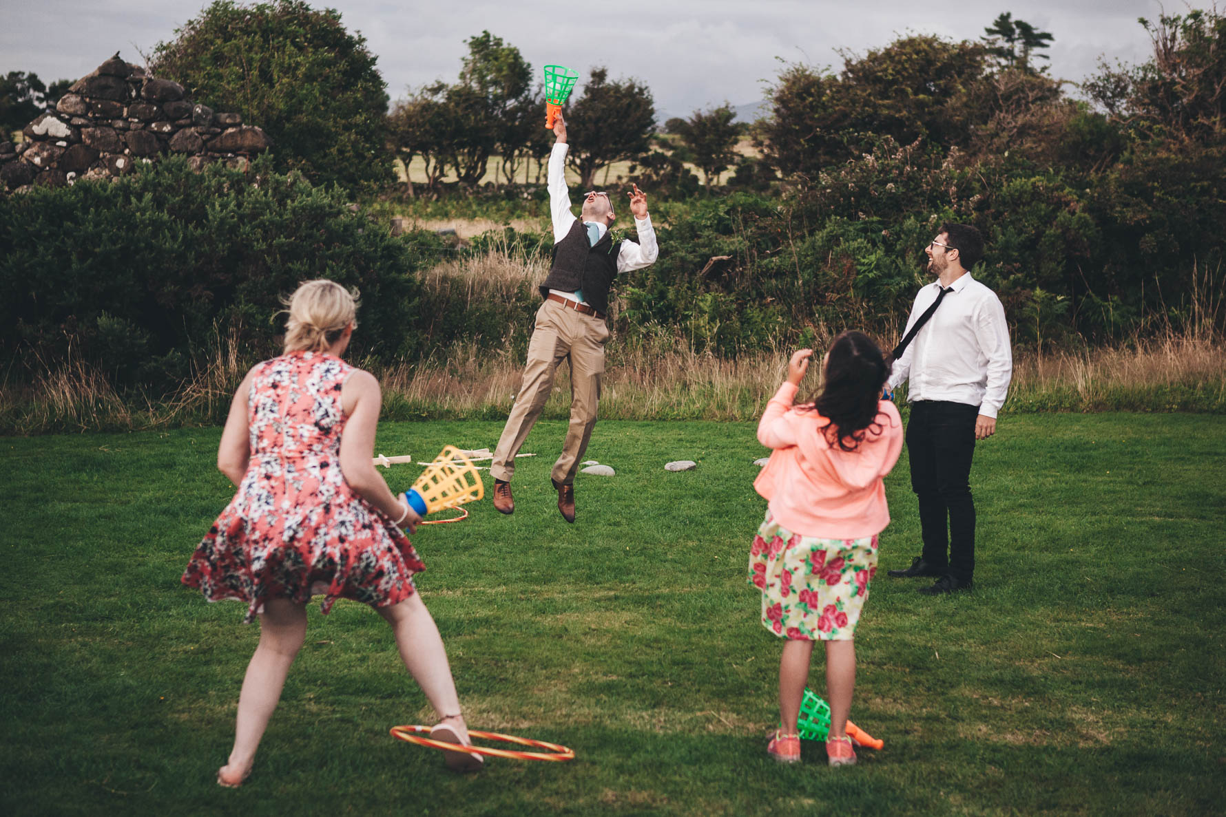 Wedding guests playing a game of catch with a male guest jumping up in the air to catch a ball in a large orange and green cone shaped device