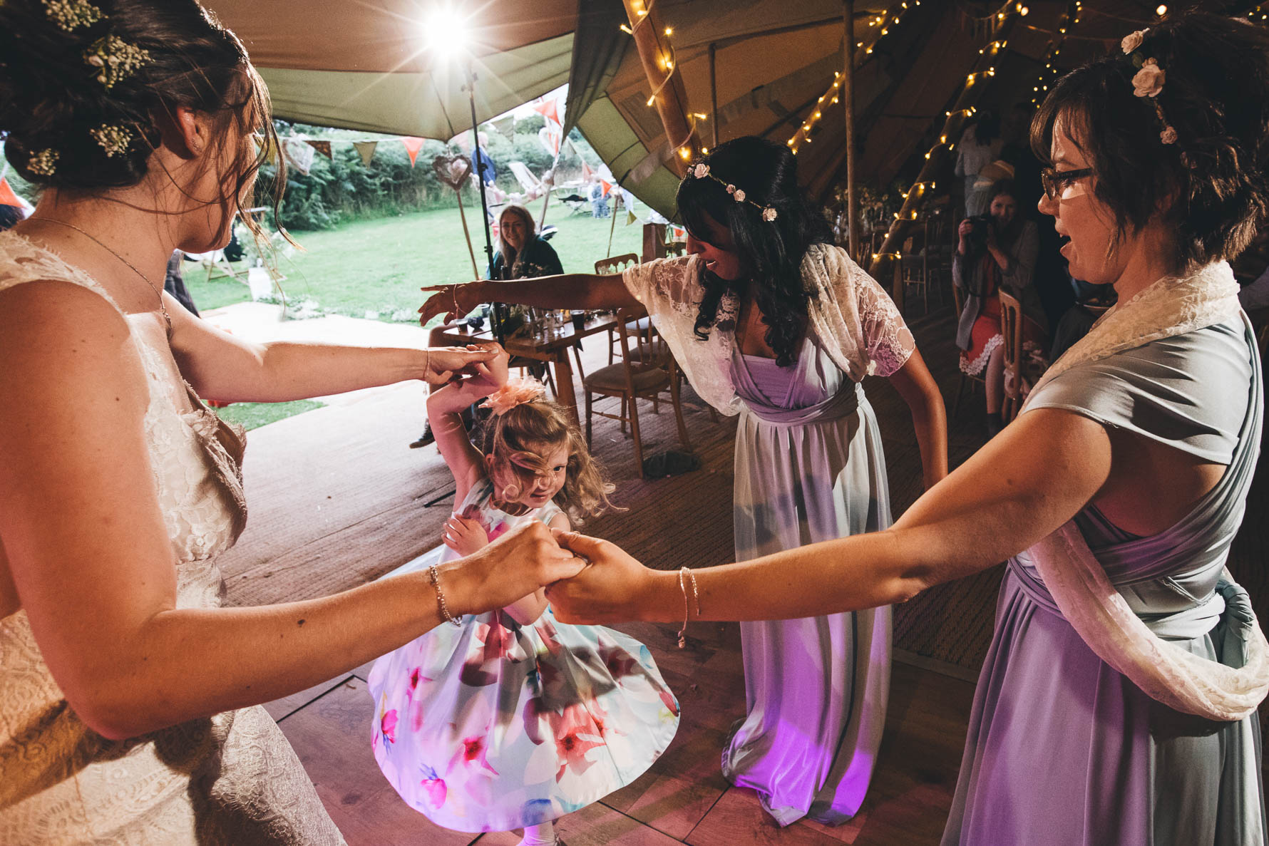 Young girl dancing with the bride and two bridesmaids inside a tipi at Red Welly