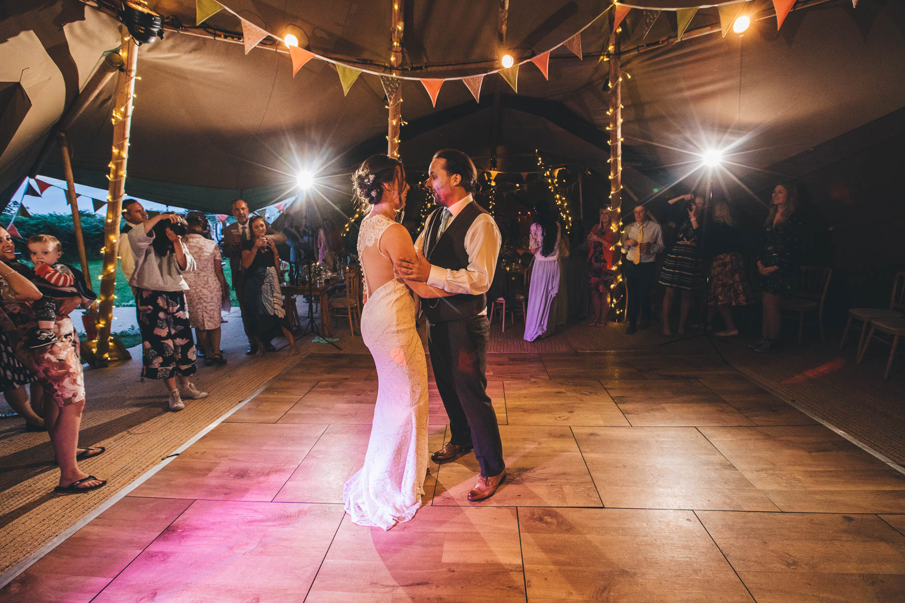 Bride and Groom with their arms around each others waist during their first dance inside a tipi with bunting and fairylights in the background