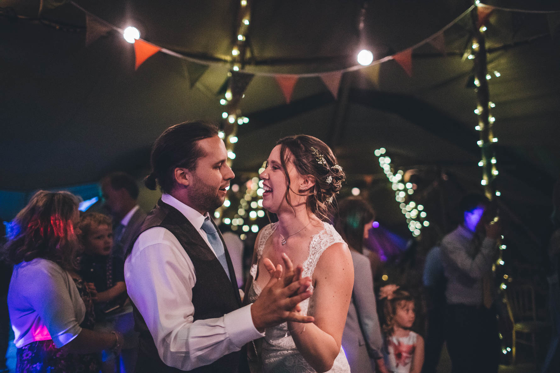 Bride and groom dancing with their hands together inside a tipi with bunting and fairylights in the background
