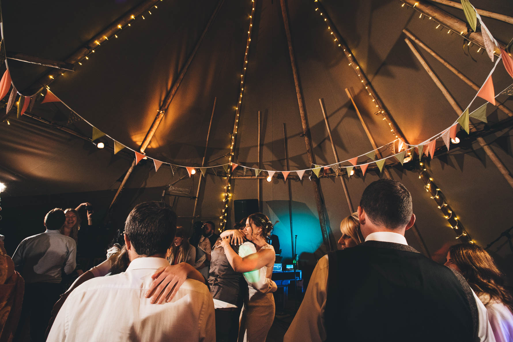 Bride and groom hugging each other on the dancefloor inside a tipi at Red Welly with bunting and fairylights draped around the supports of the tipi