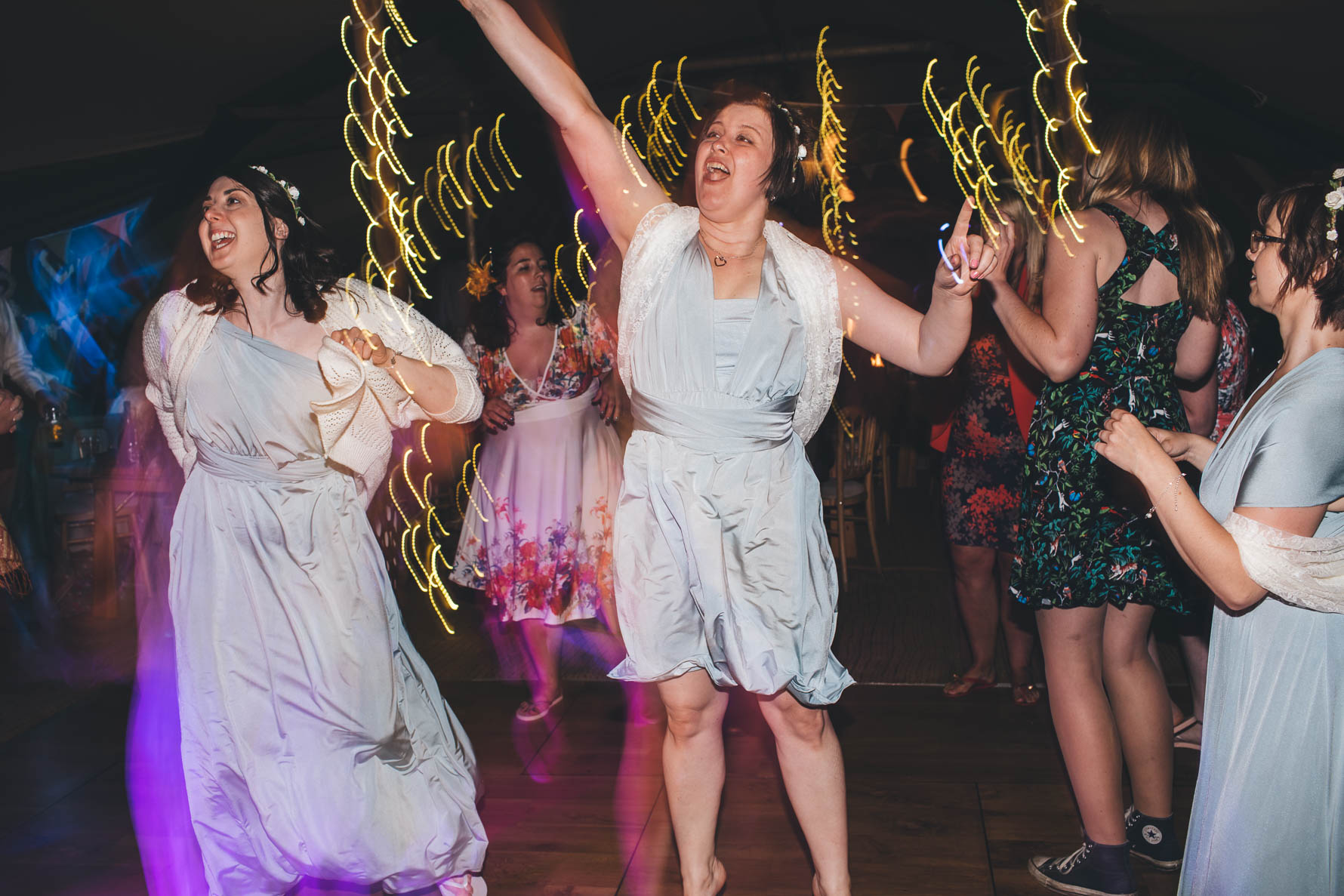 Bridesmaid jumping in the air on a dancefloor as she sings along to a song with blurred lights in the background