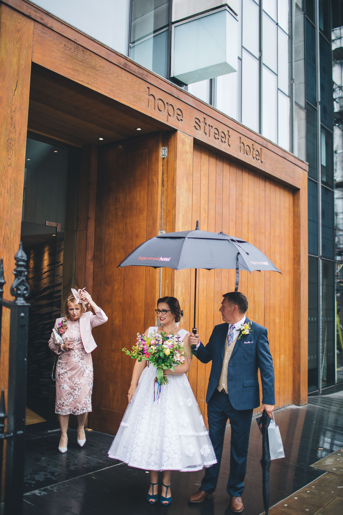 bride and father wating in rain under an umbrella outside their hotel