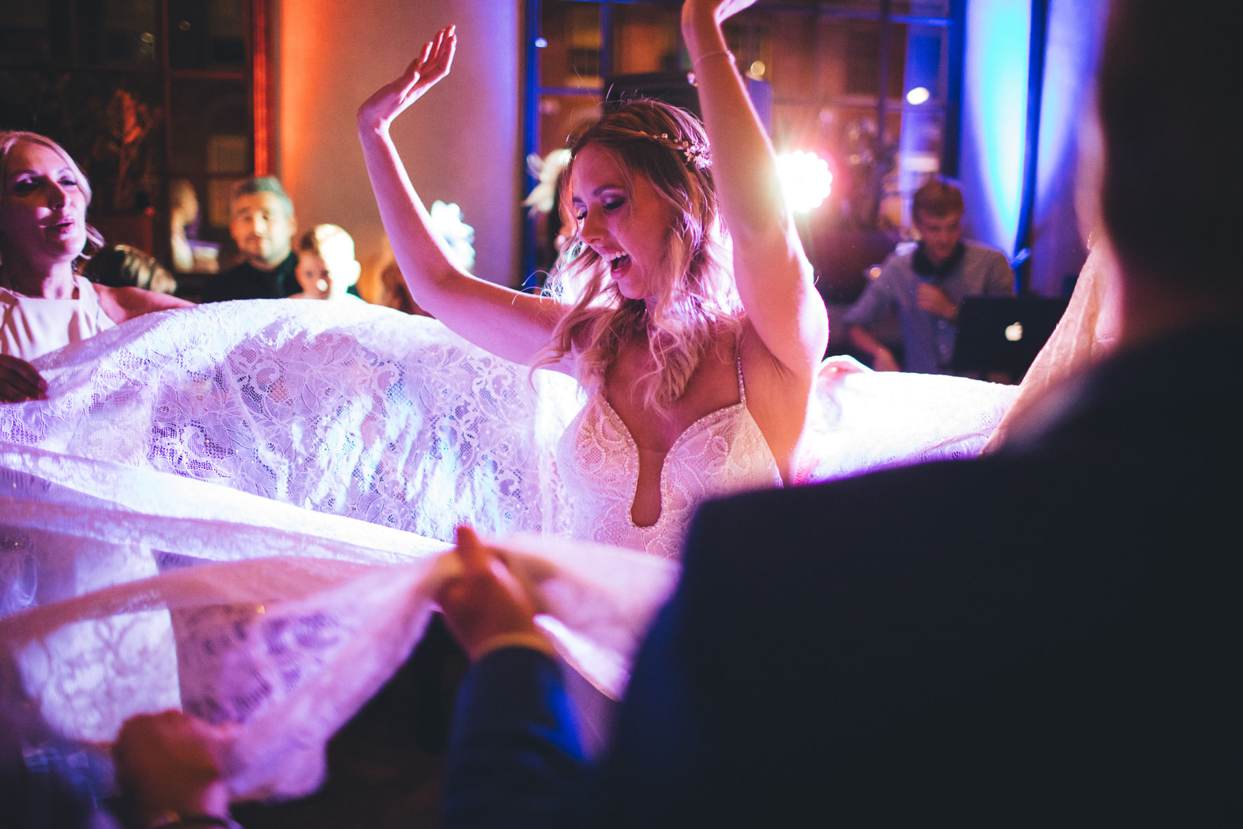 bride twirls as guests hold up her dress on the dancefloor