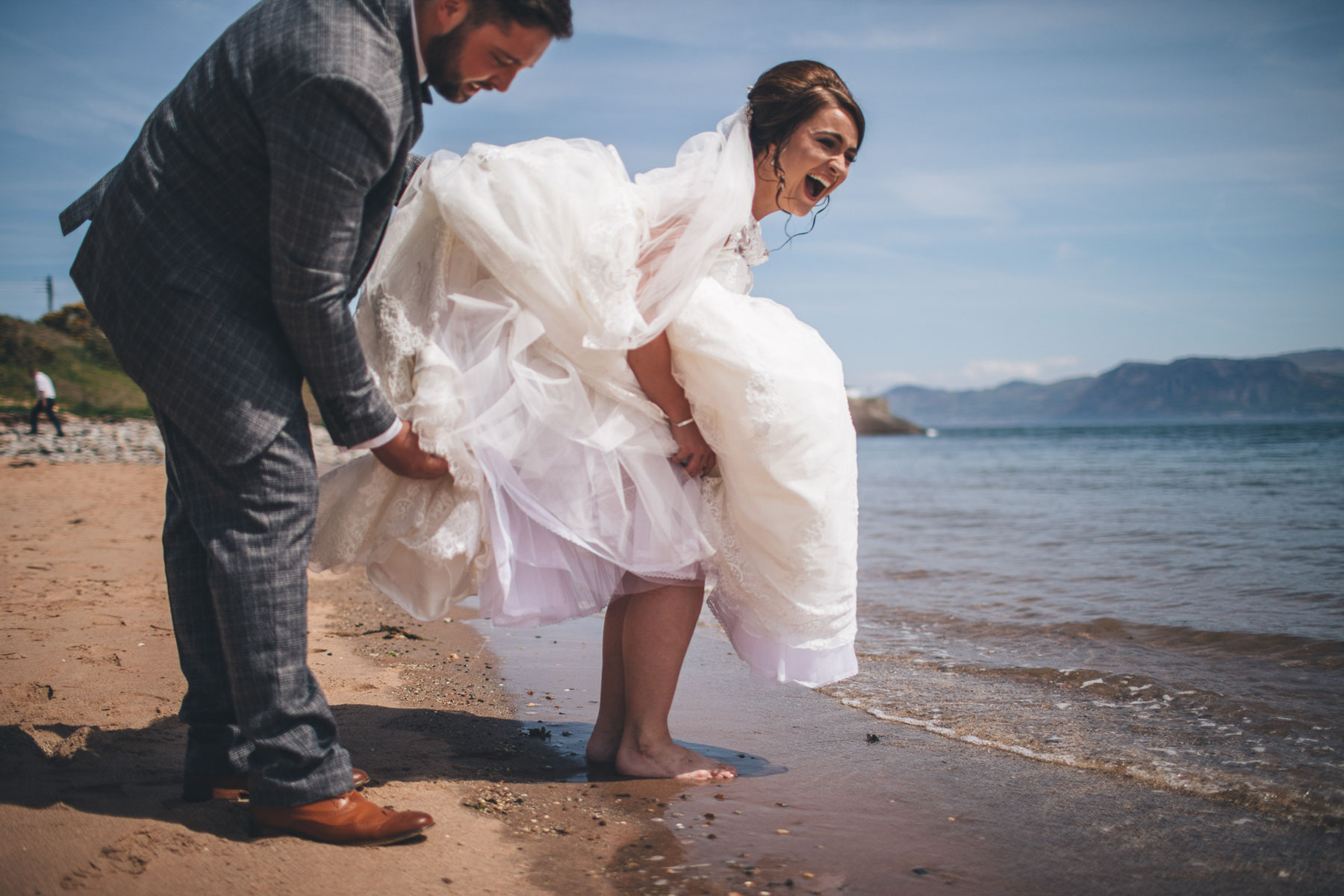 bride laughs as she steps into the sea in her big wedding dress