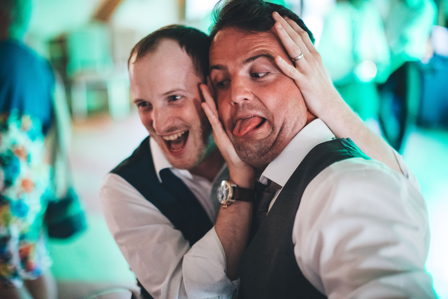 man pulls silly face with his friends hands on his ears