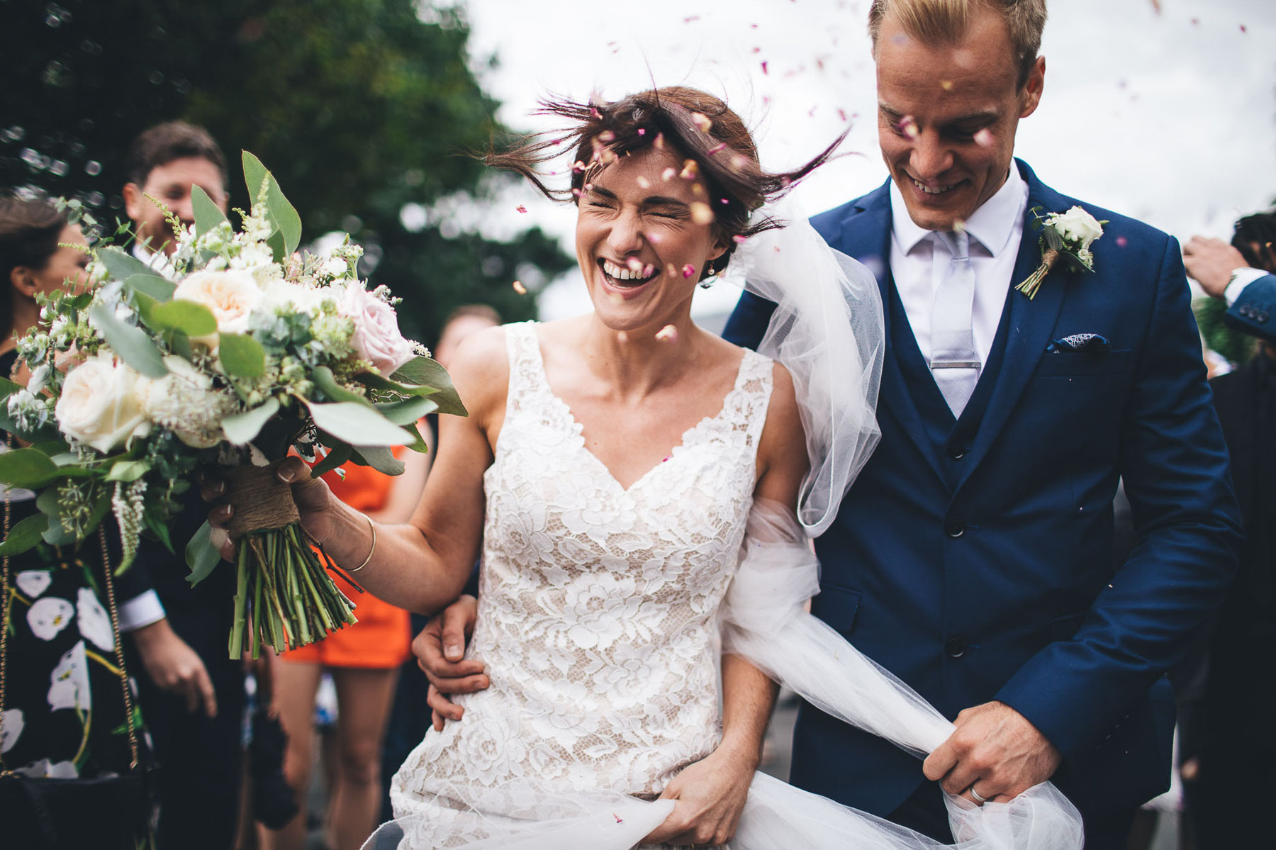 confetti moment that was very windy, the brides hair is lifted up and her eyes are tightly closed as she laughs