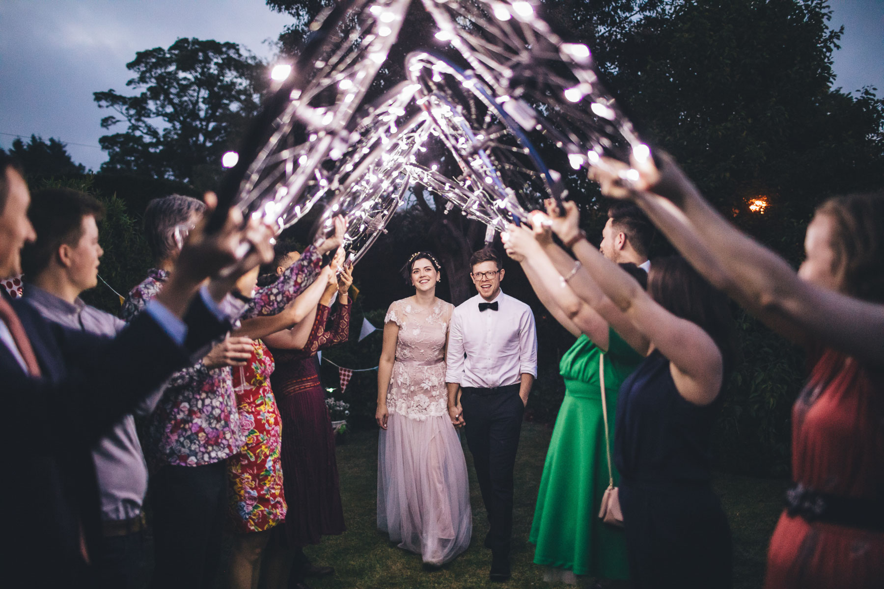 couple walk underneath archway of bike wheels covered in fairy lights