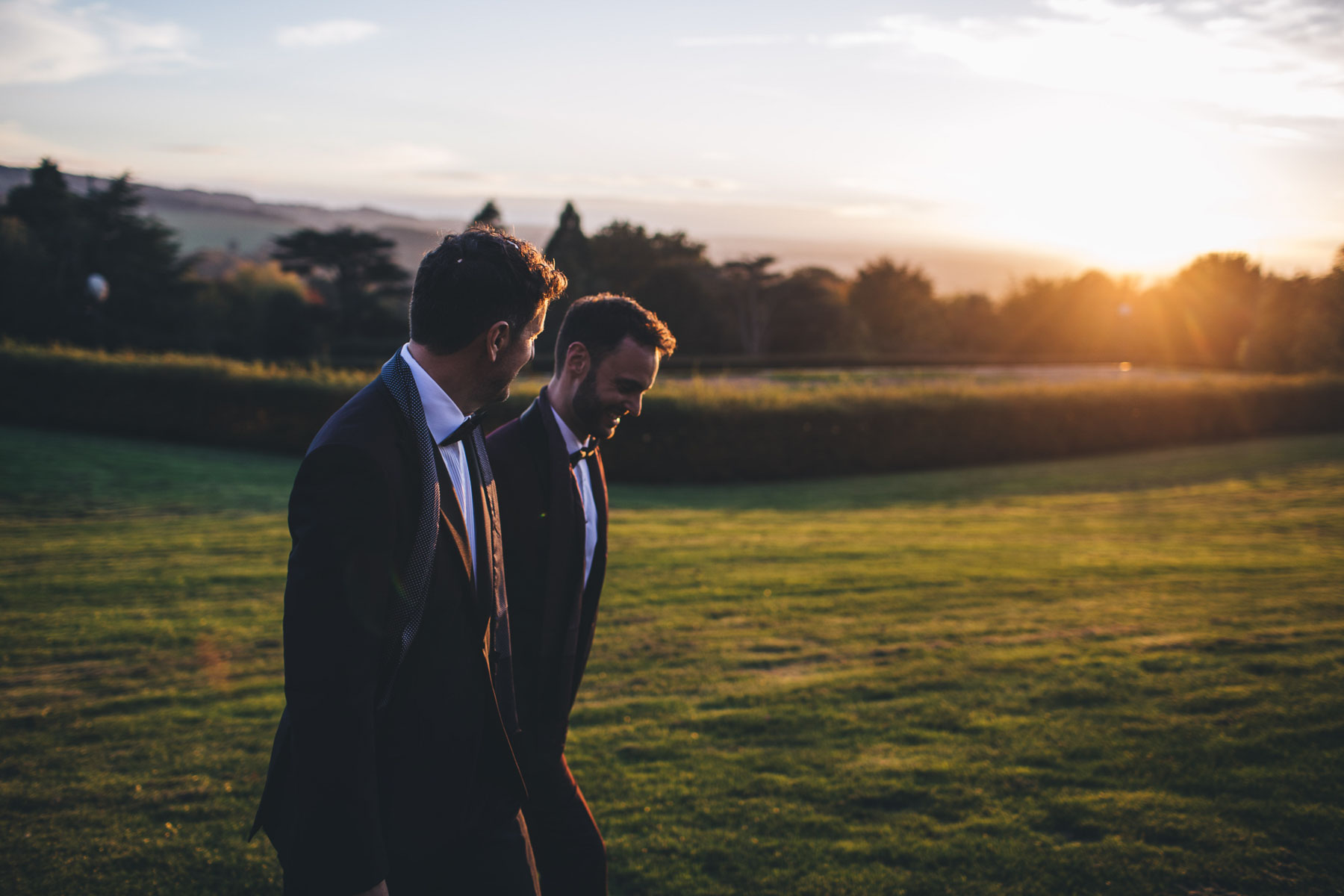 two grooms take a walk together during a golden sunset