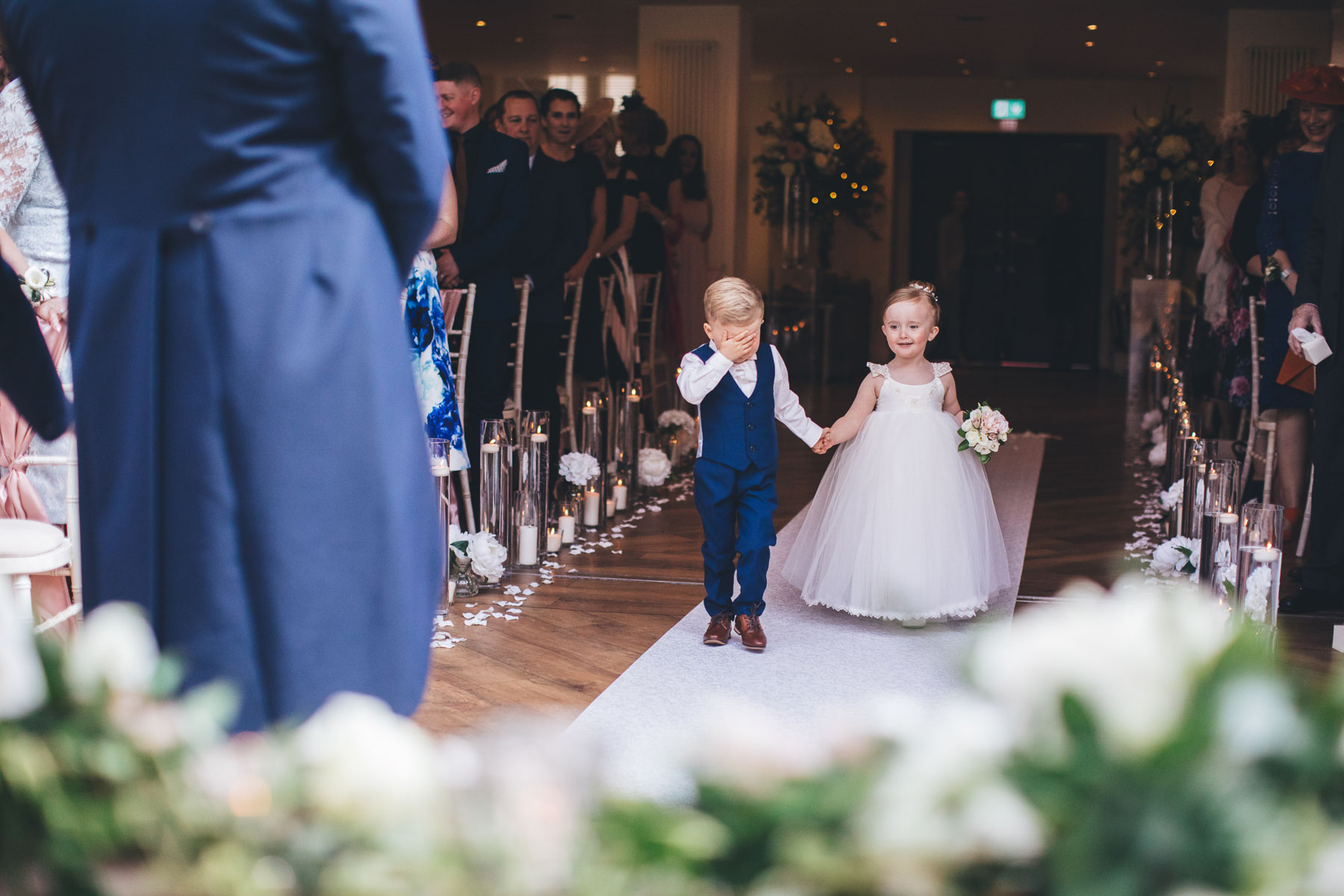 boy covers his face coming down the aisle with a flower girl