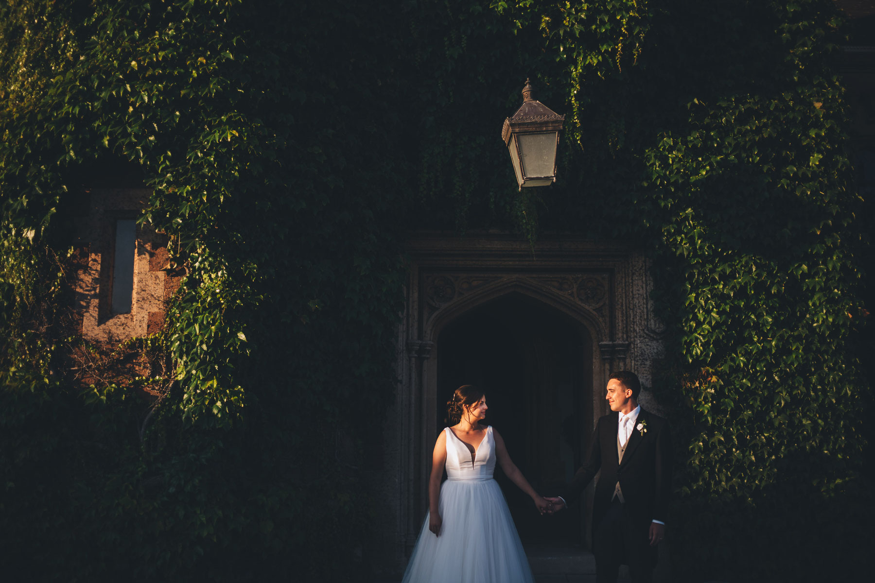 couple look longingly at each other during the last of the evenings beautiful sunset light, they stand in front of a ivy covered building