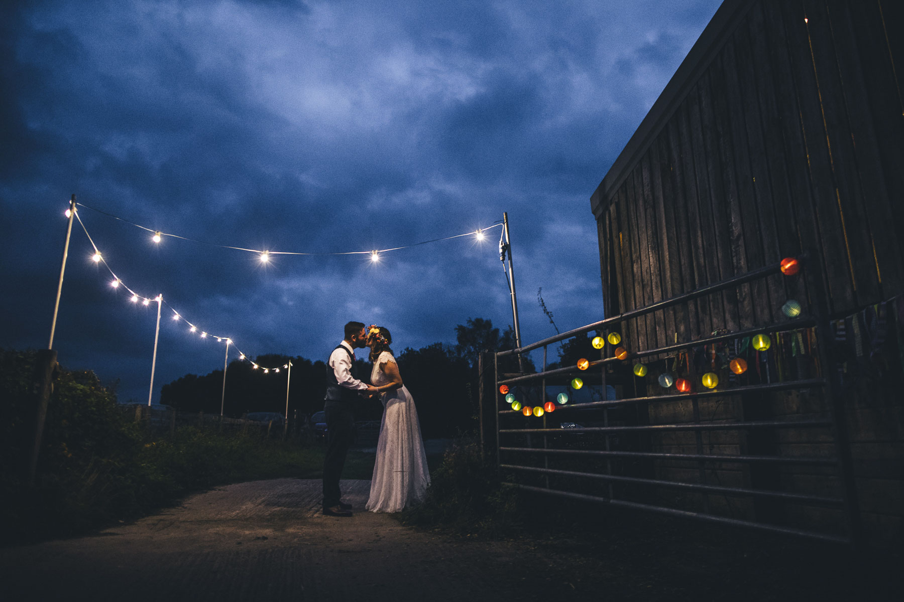 couple kiss under festoon lights in a barn style wedding