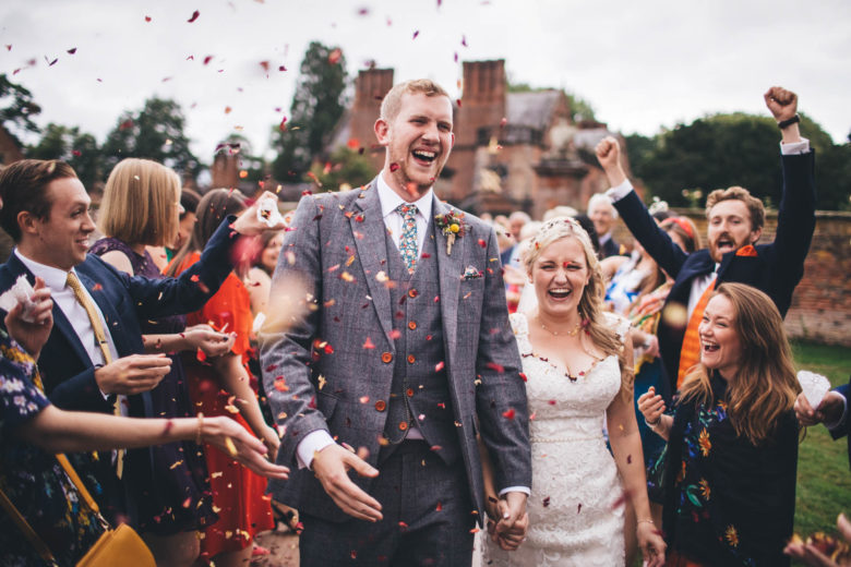 happy faces and arms in the air as the couple walk through a sea of confetti