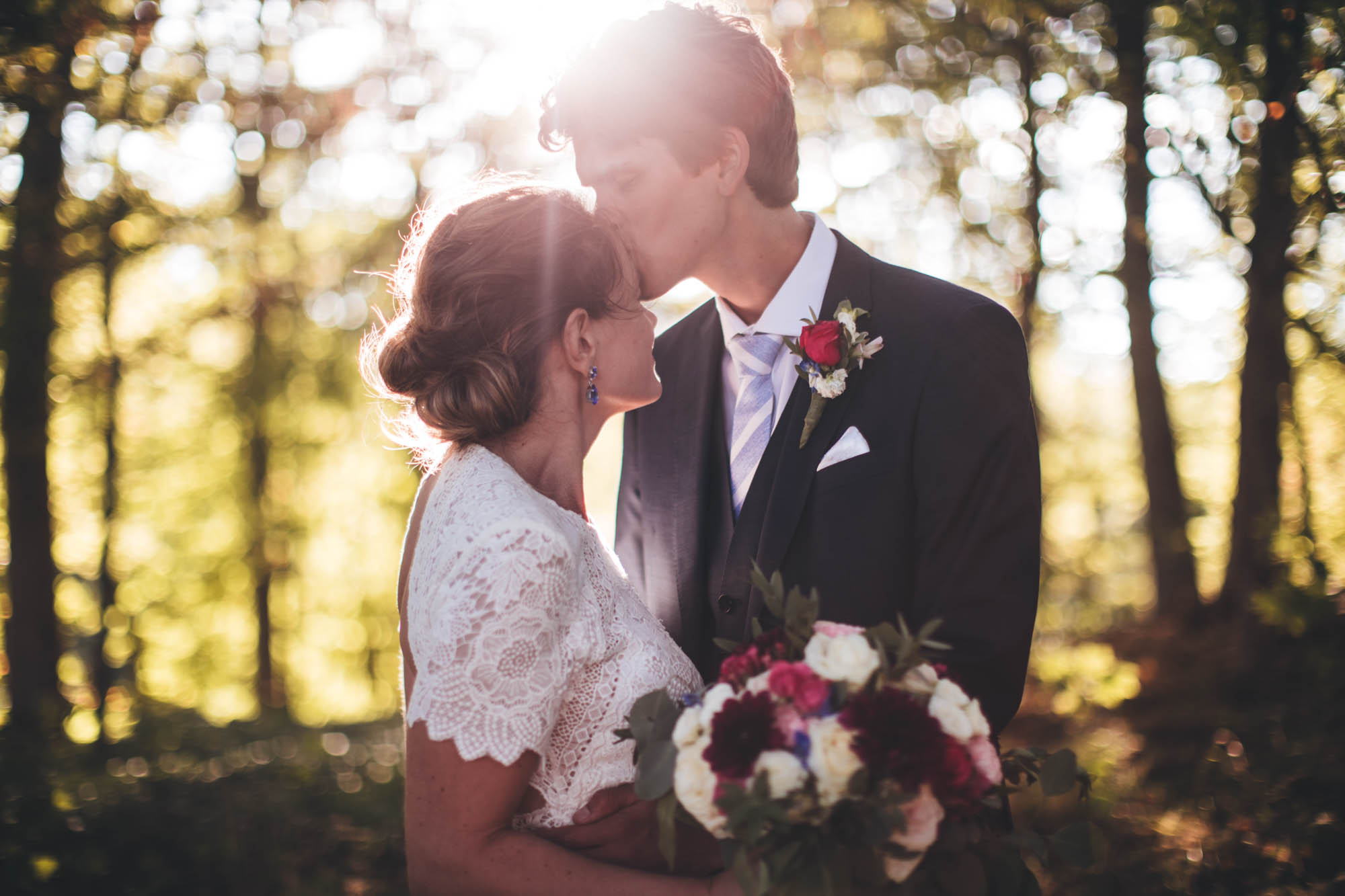 groom kisses brides forehead back lit by the evening sunshine