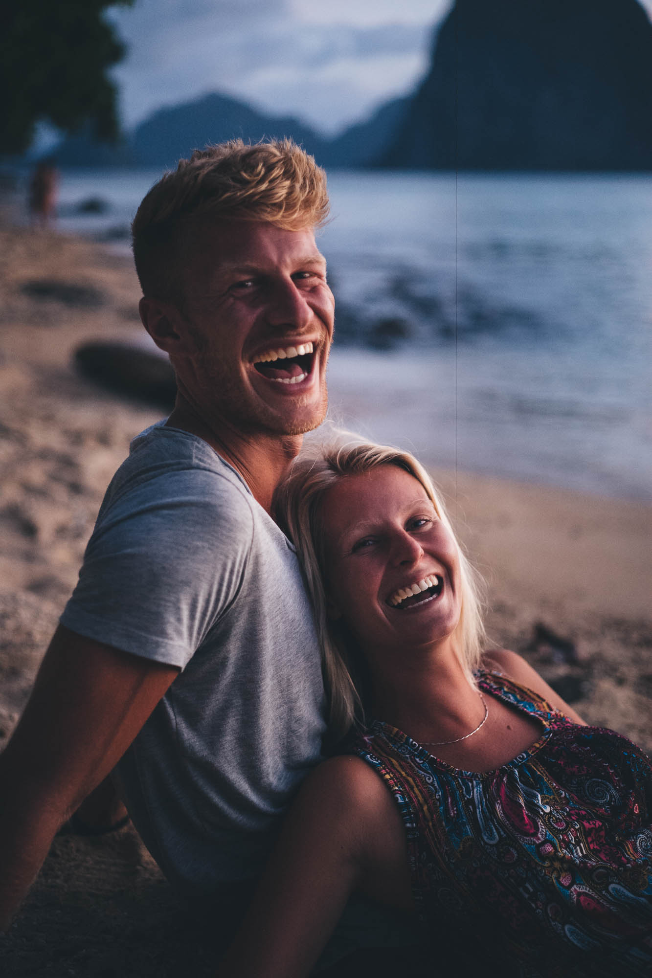 huge smiles on couples faces as they sit together at the beach a sunset
