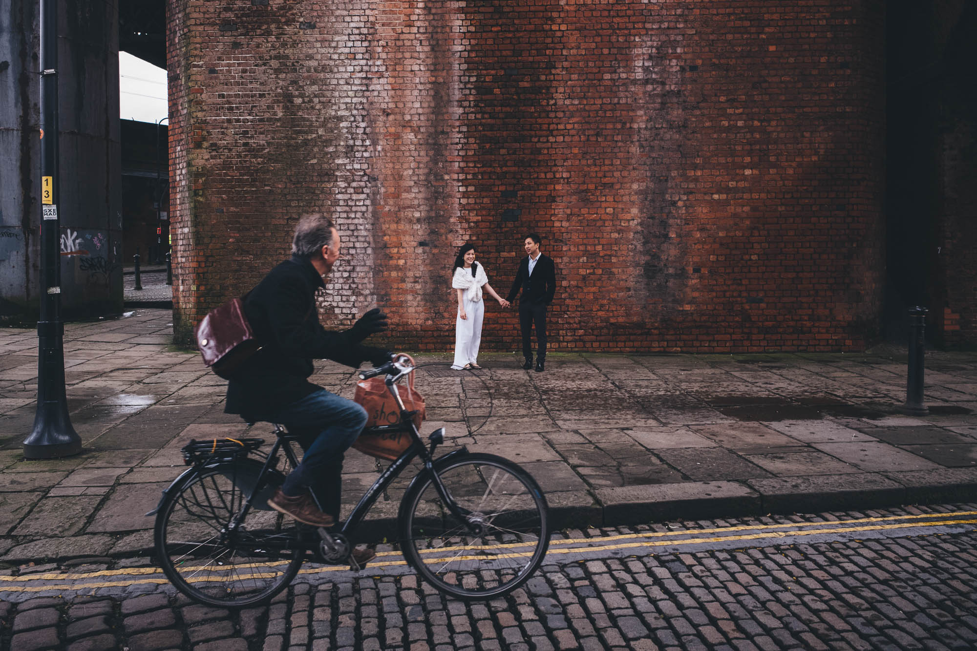 cyclist photo bombs a couple against a brick wall in castlefield manchester