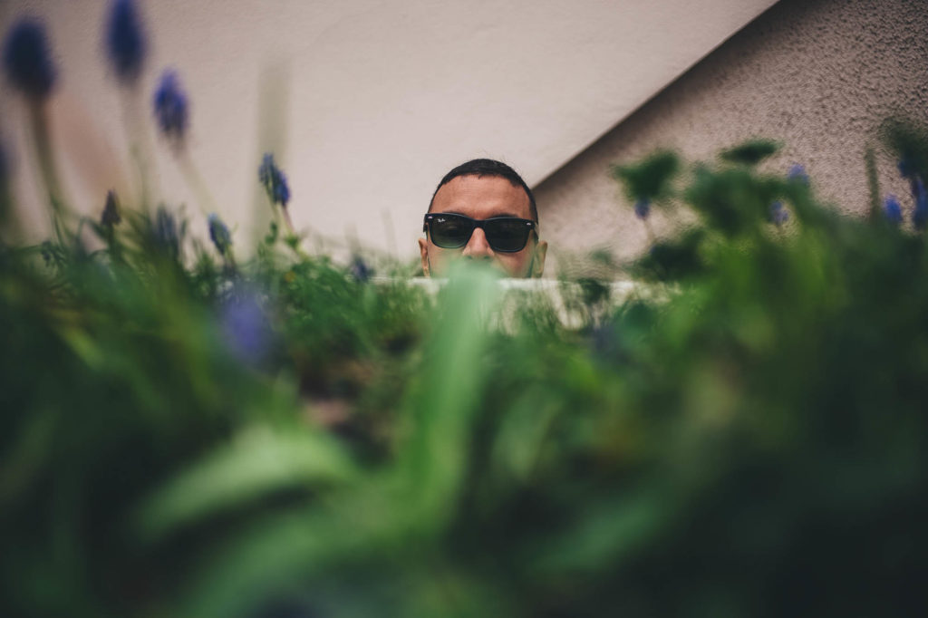 a cheeky funny portrait of man in sunglasses behind some plants