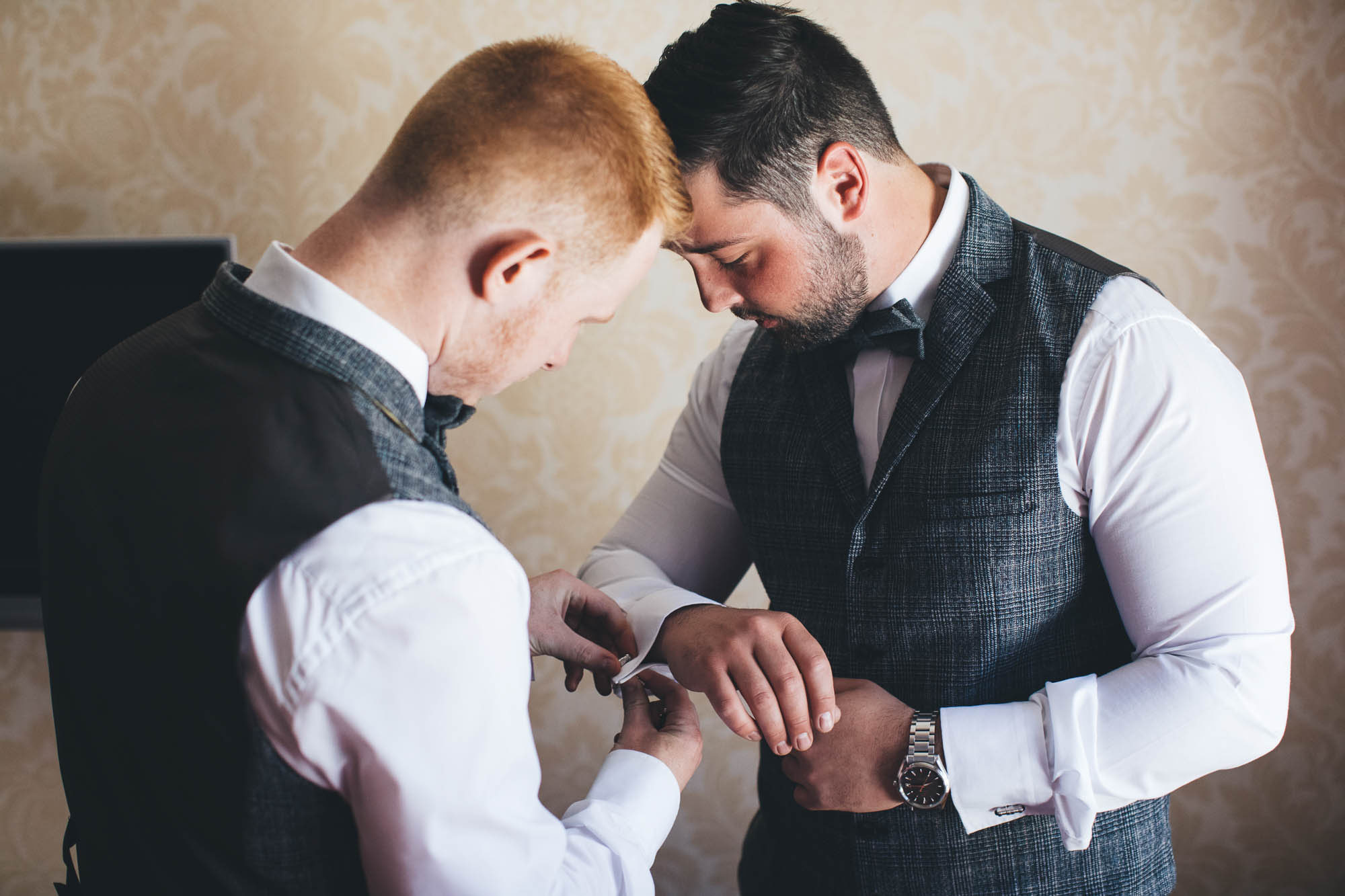Groomsman helps Groom with his cuff-links on morning of wedding