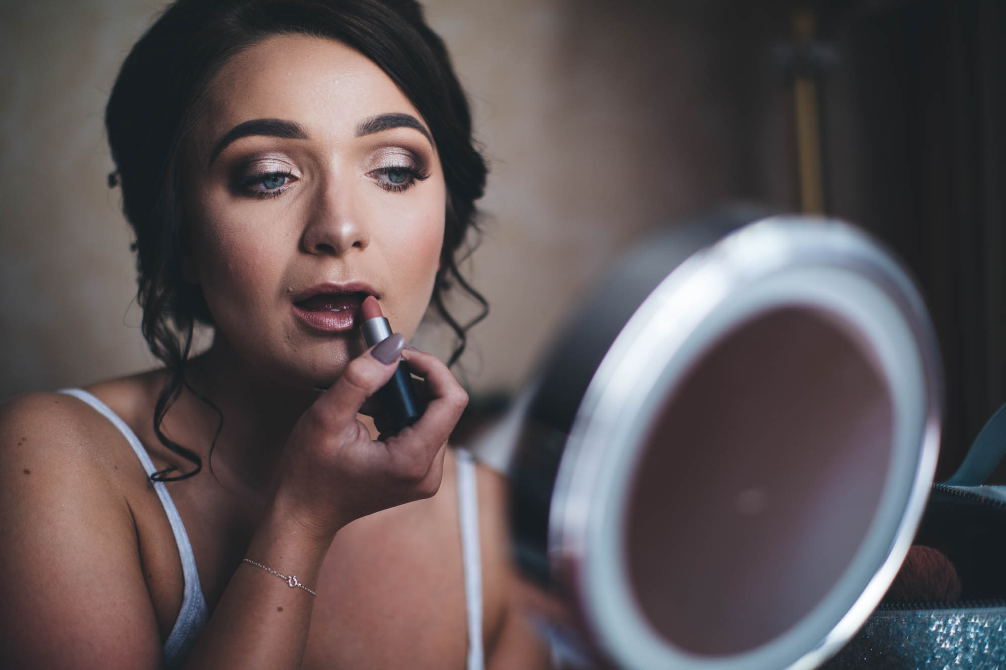 Bride applies lipstick whilst looking in mirror during bridal preparations