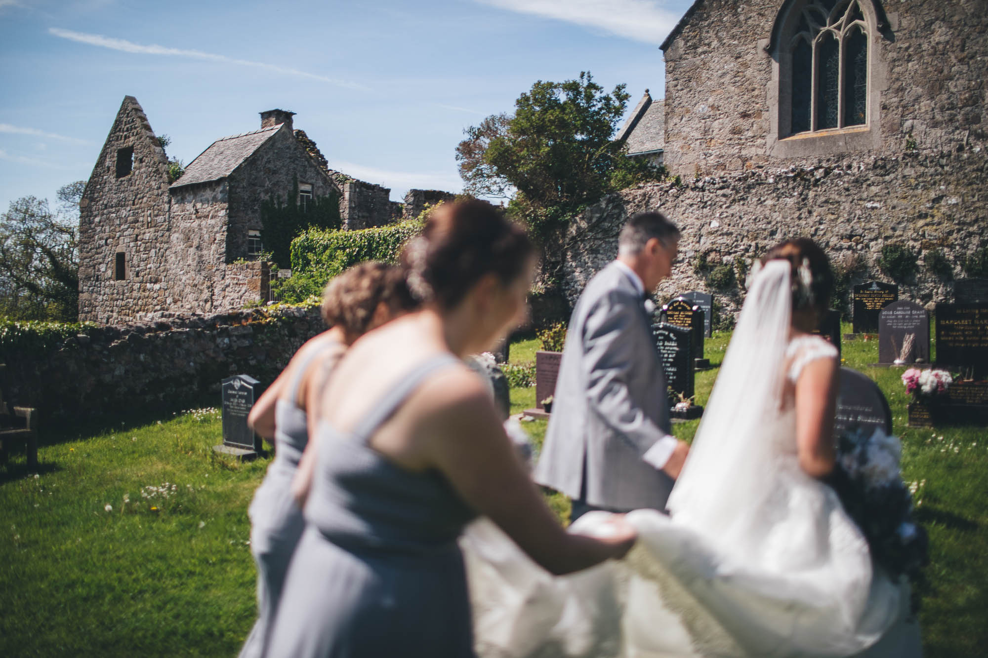 Bridesmaids help to carry Bride's wedding dress train as they walk towards the church