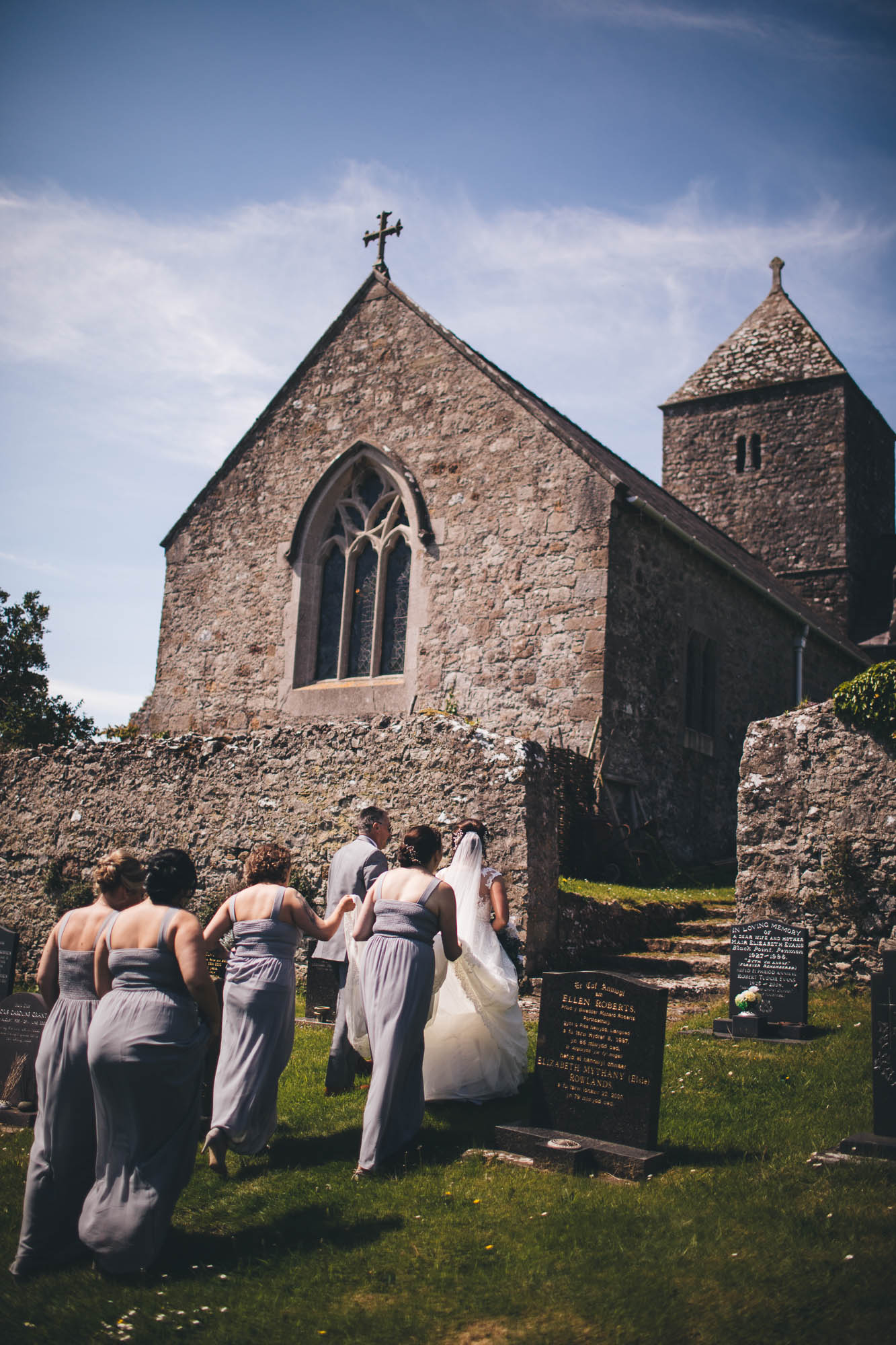 Bride and Father of Bride lead procession through garden into historic Anglesey Penmon church