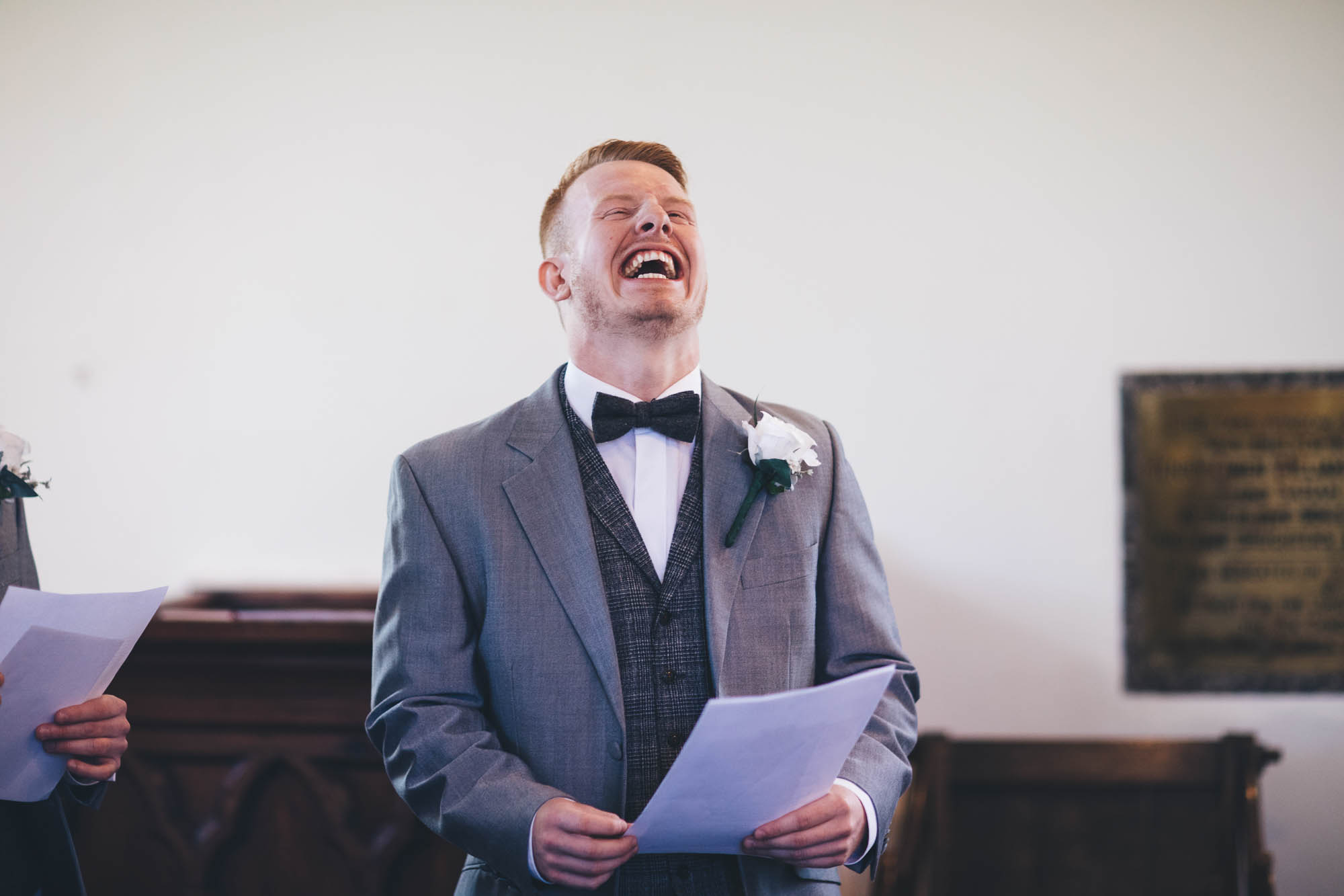 Groomsman laughs whilst he holds a piece of paper waiting for the wedding ceremony to start